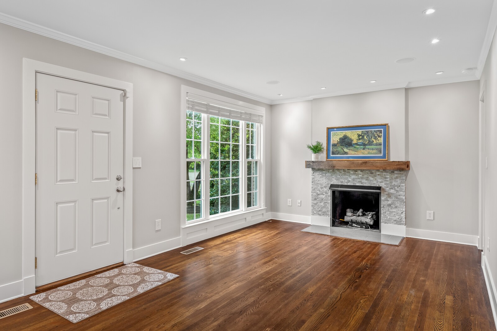 Bright entry room with a stone fireplace, large window, and dark hardwood floors.