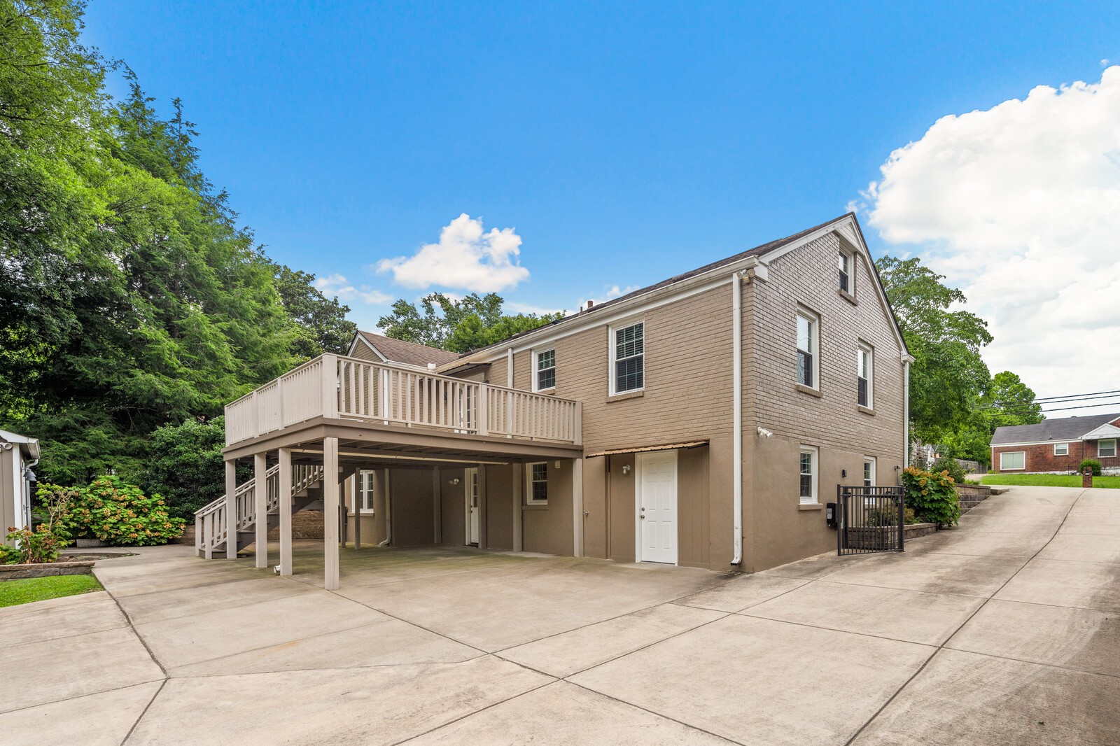 Two-story tan brick home with an elevated deck and broad concrete driveway.