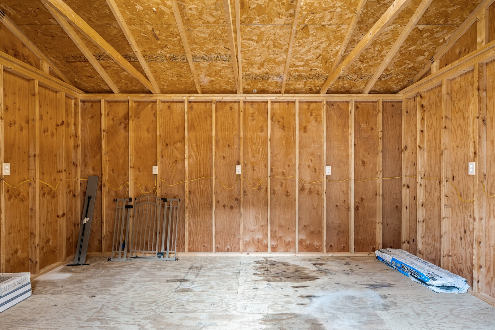 Unfinished garage with exposed plywood walls, ceiling framing, and electrical wiring.