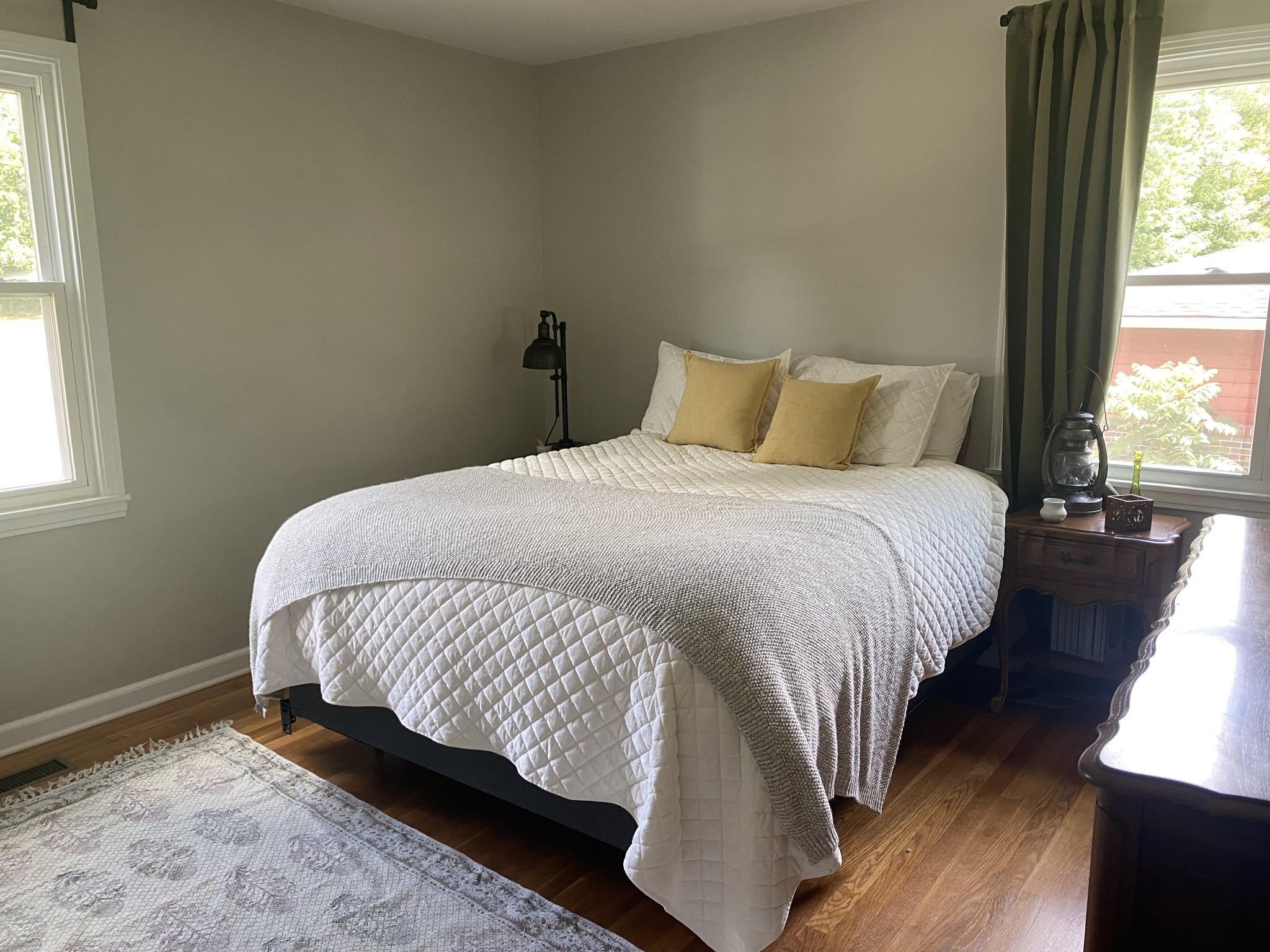 Bedroom with a white quilted bed, mustard pillows, hardwood floors, and two windows.