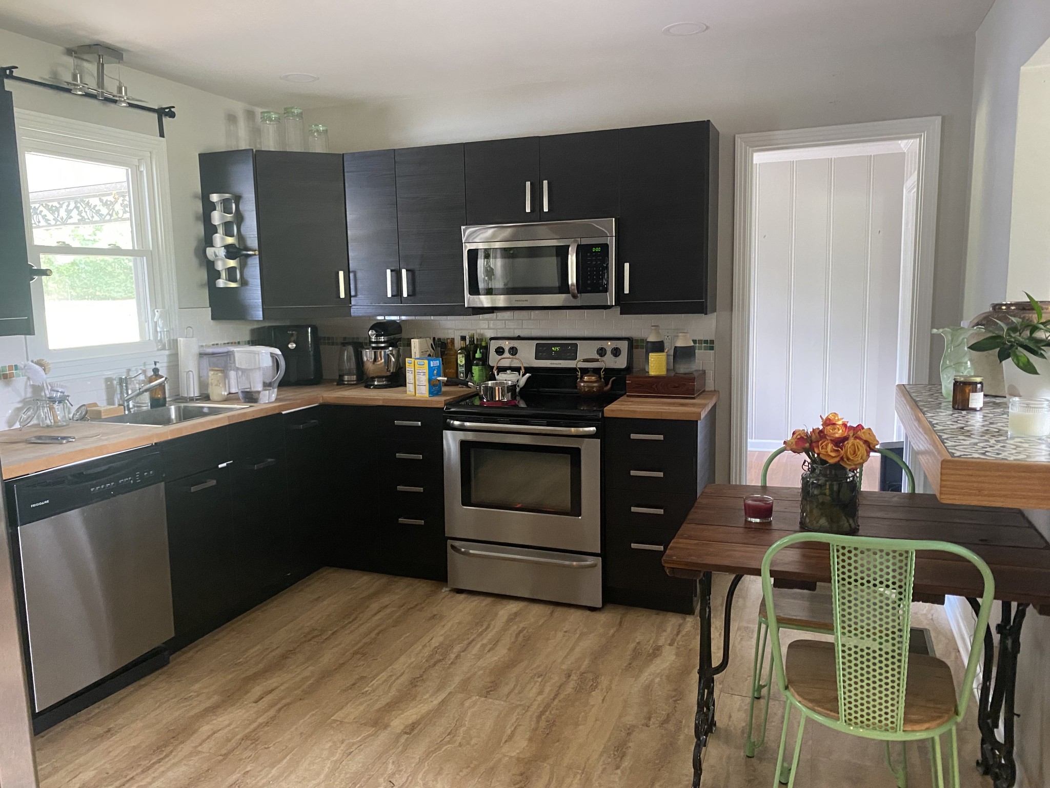 Kitchen with dark cabinetry, stainless steel appliances, and a wood dining table with green chairs.