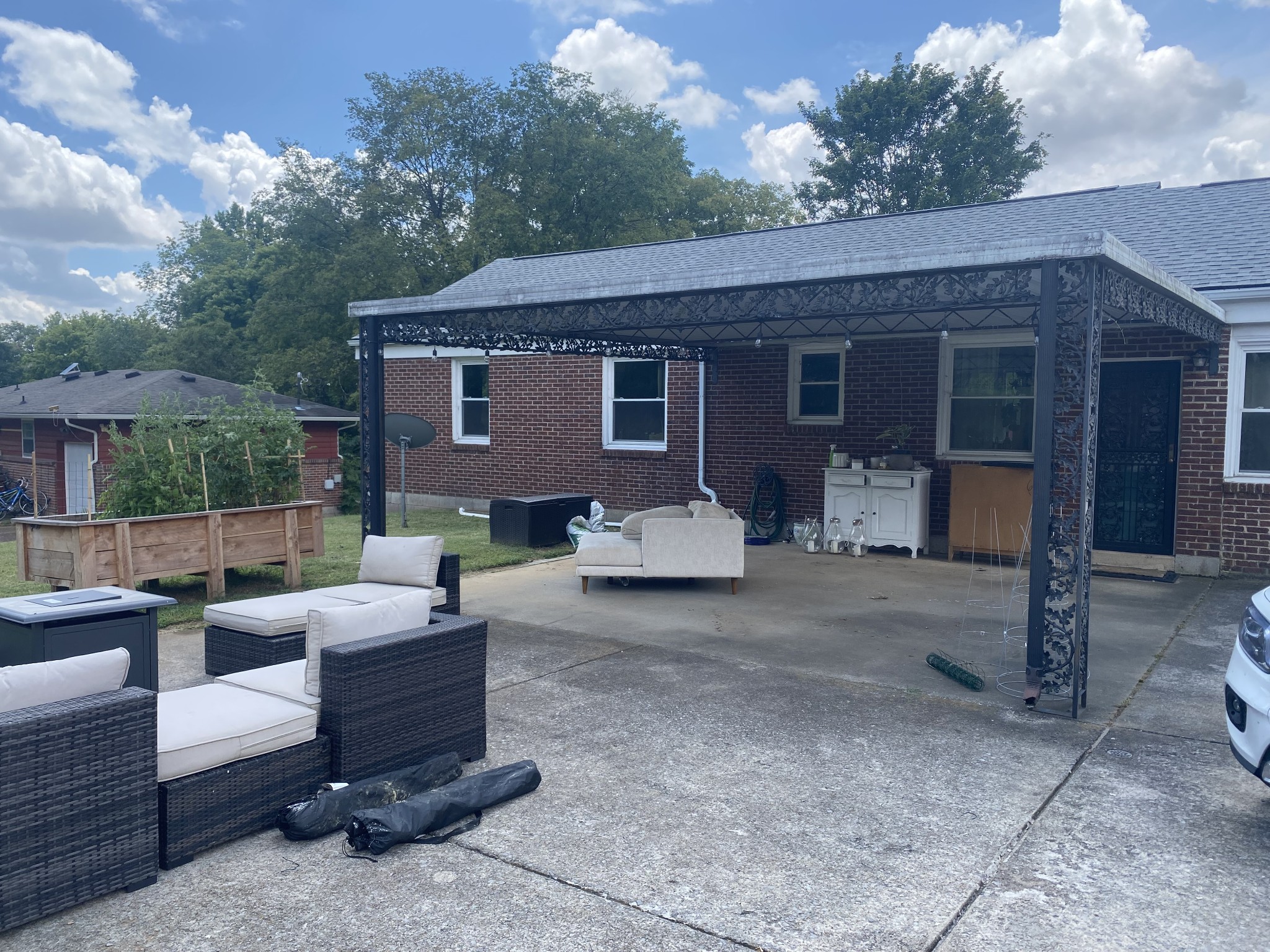 Brick home’s covered back patio with ornate pergola, outdoor seating, and raised garden beds.