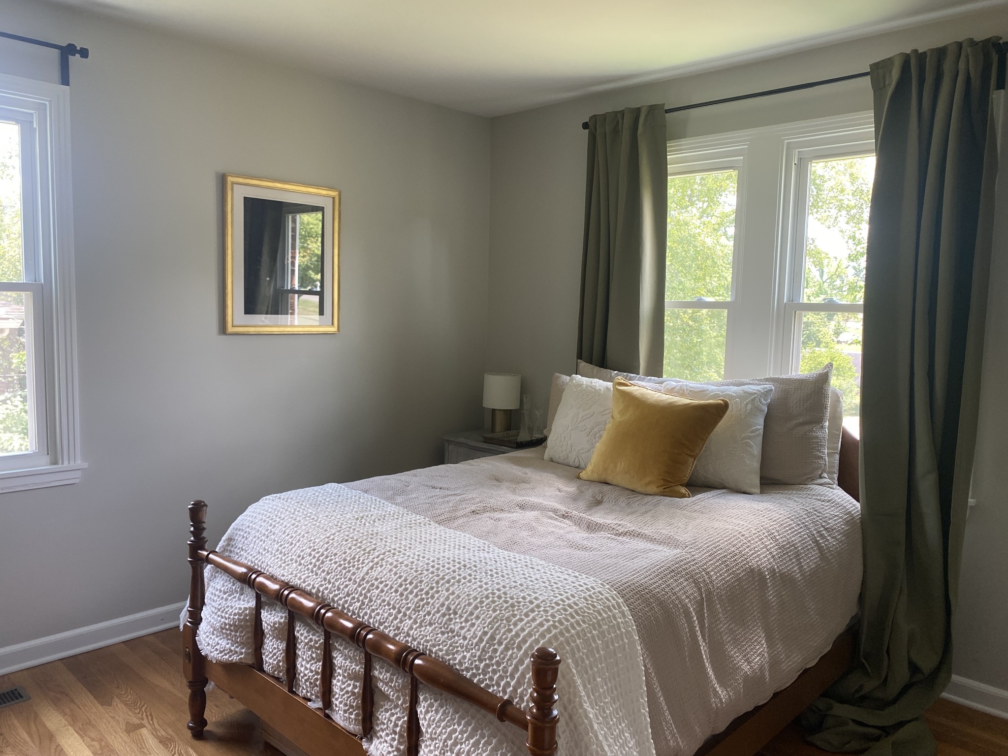 Furnished bedroom with white textured bedding, a mustard pillow, and large curtained windows.