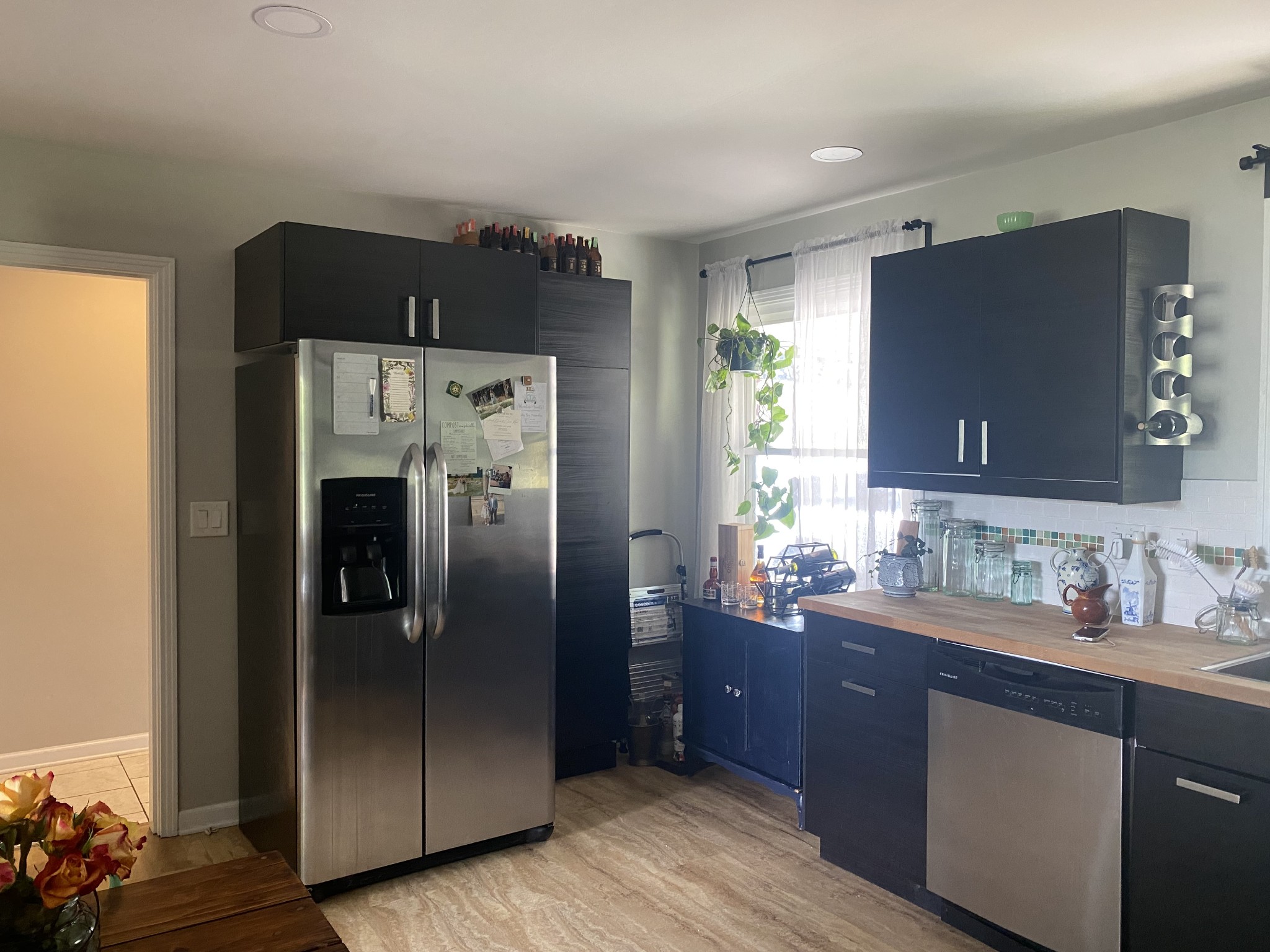 Kitchen with dark cabinets, stainless-steel appliances, wood countertops, and a bright curtained window.