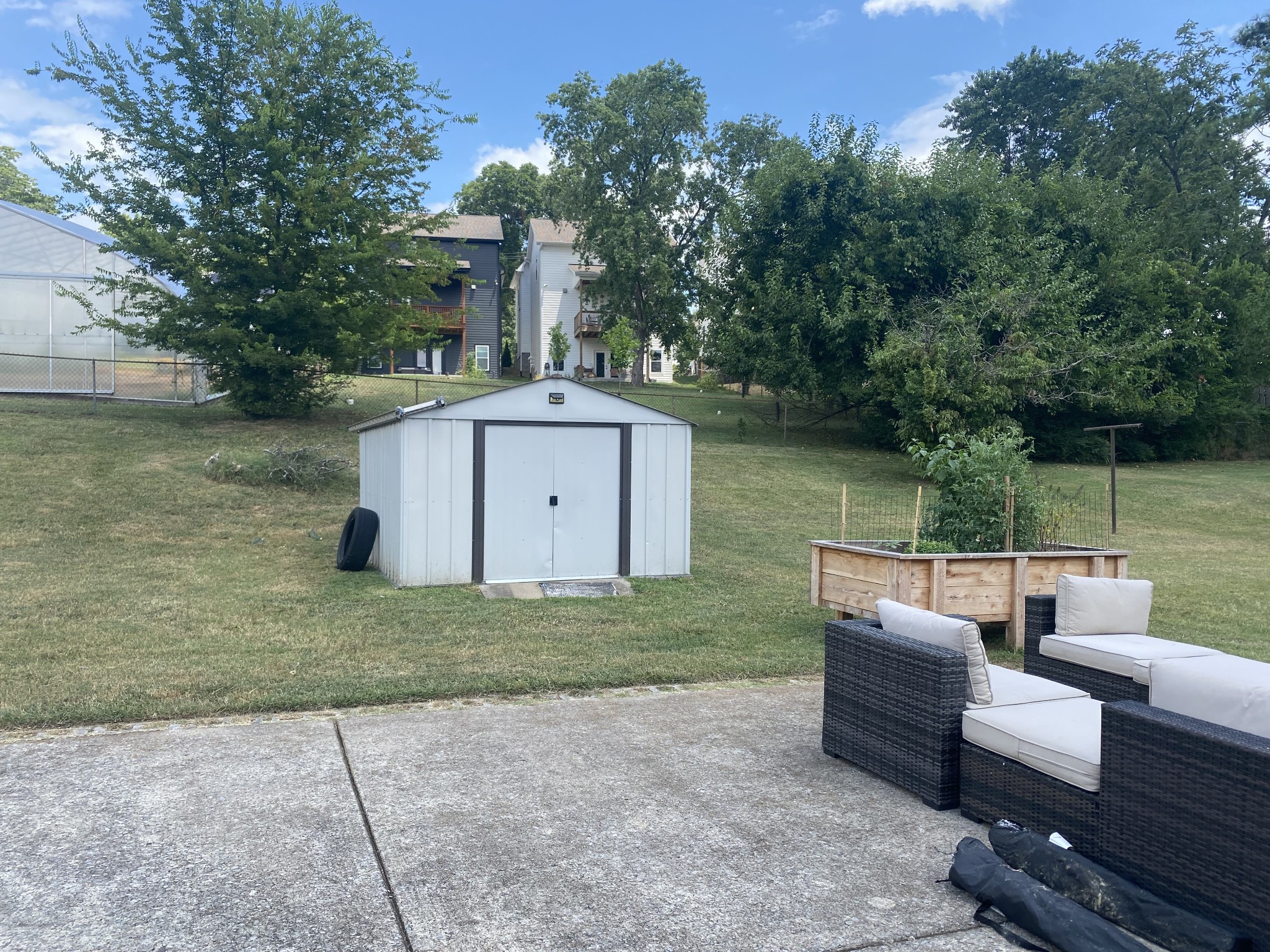 Backyard patio with outdoor seating, a raised garden bed, lawn, and storage shed.