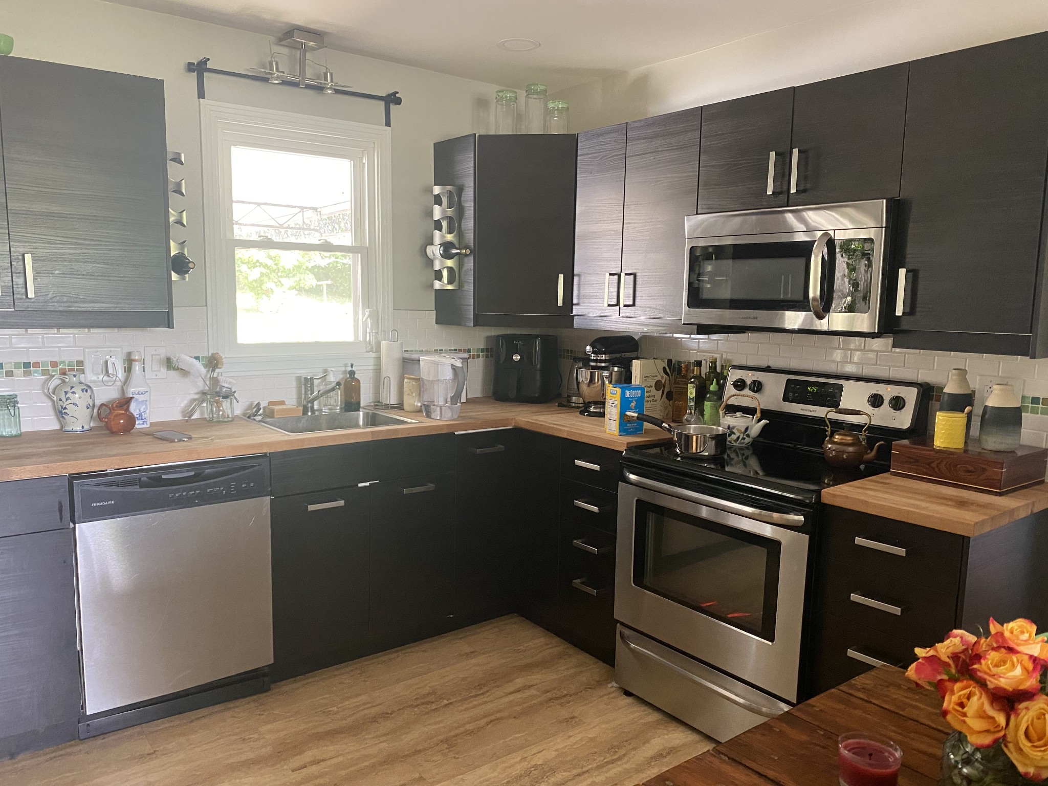 Kitchen with dark cabinets, butcher-block counters, stainless appliances, and a sink below the window.