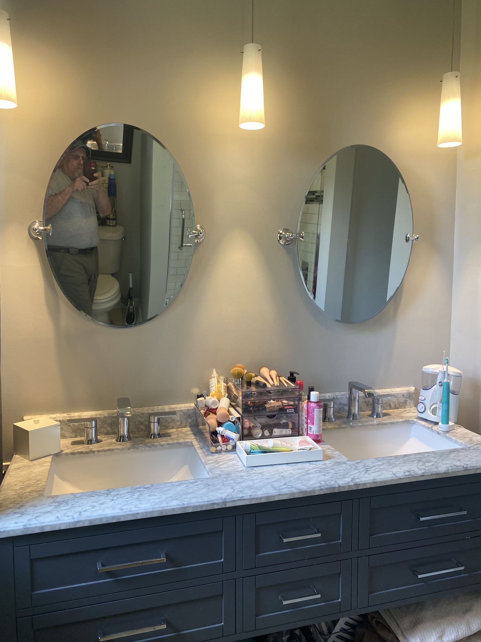 Bathroom vanity with double sinks, marble countertop, dark cabinetry, and oval mirrors.