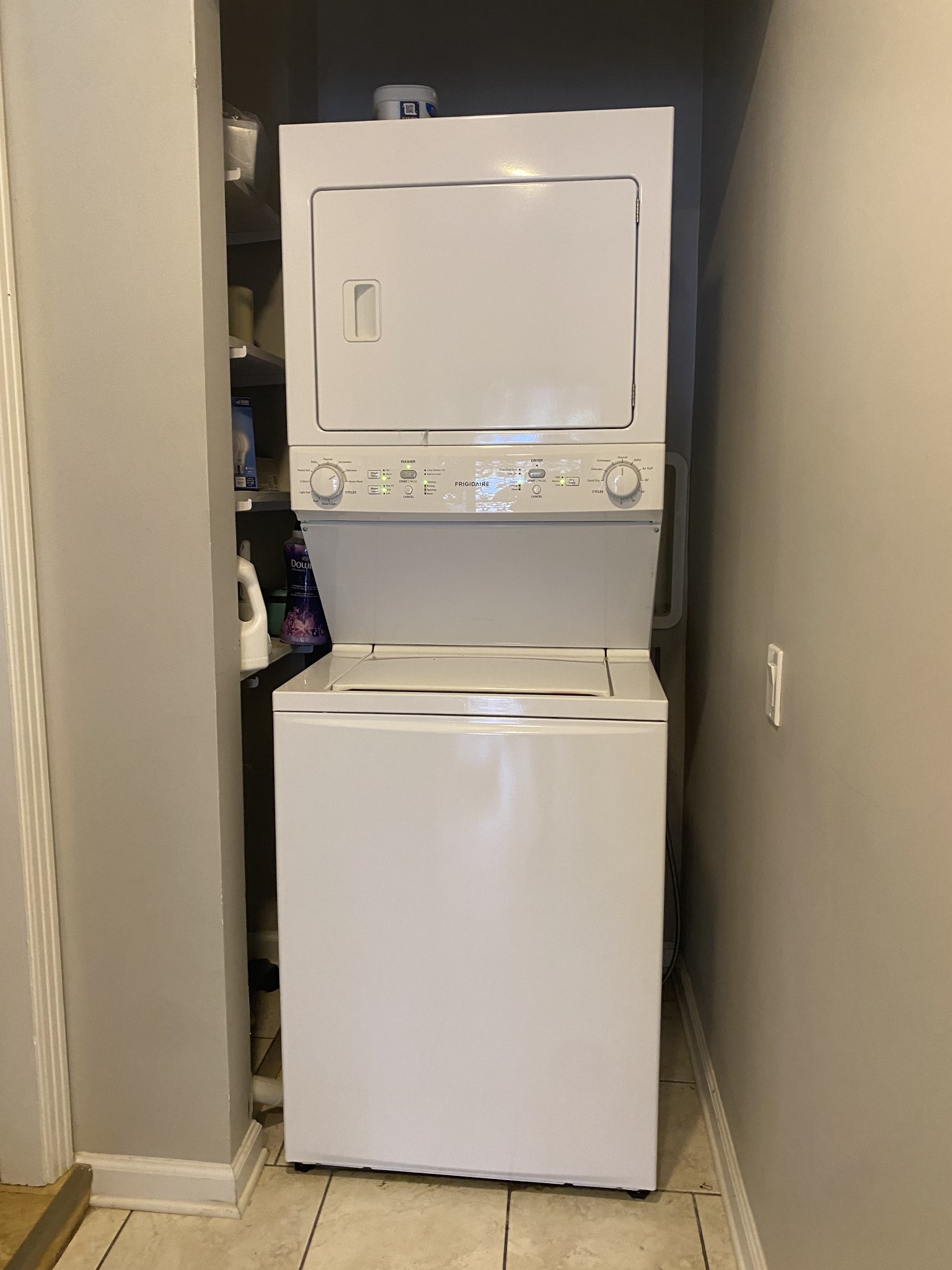 Stacked washer and dryer in a narrow laundry closet with detergent shelves.