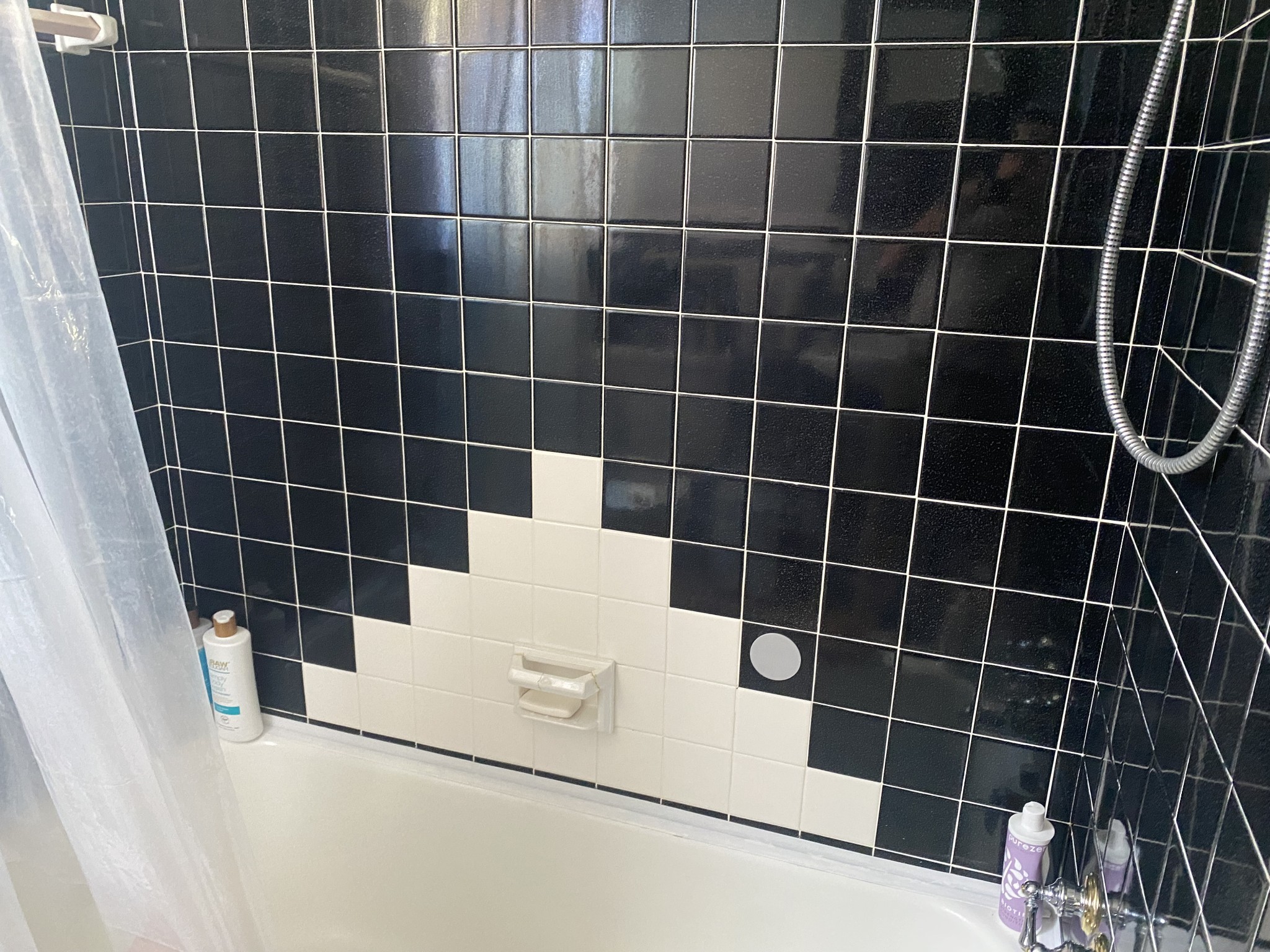 Bathtub and shower with black tile, a white geometric tile accent, and chrome fixtures.