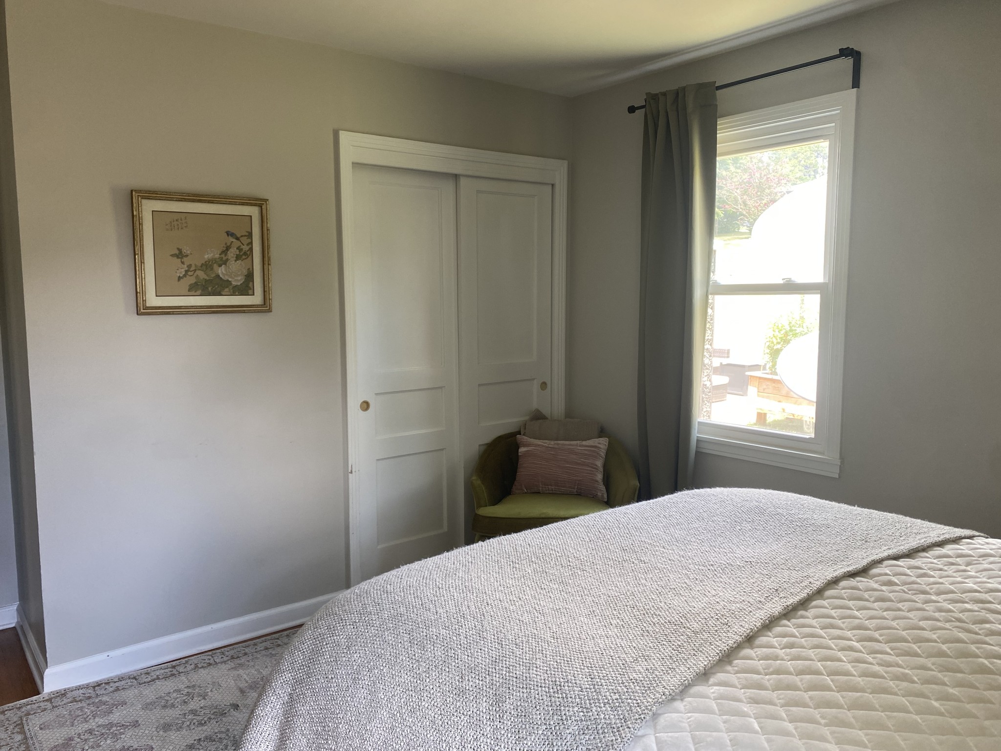 Bedroom with a textured white bedspread, green chair, paneled closet doors, and curtained window.