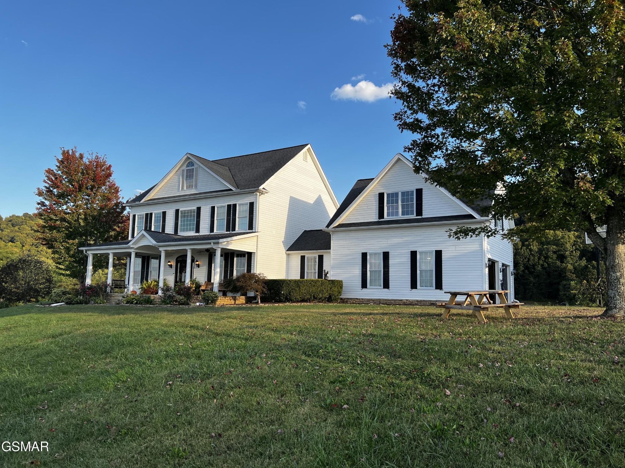 White two-story house with a covered porch, black shutters, and a broad lawn.