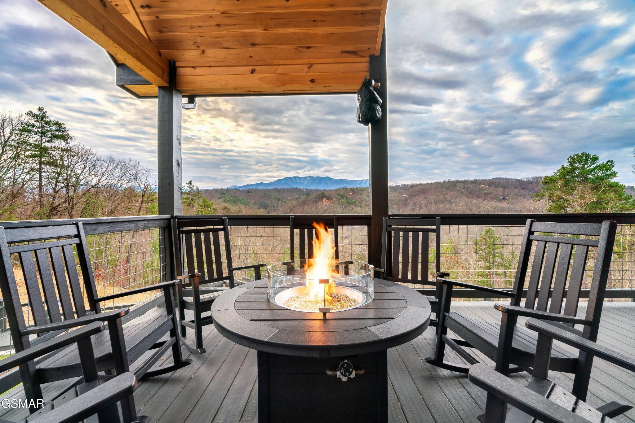 Covered deck with a round fire pit and rocking chairs overlooking mountain ridges.