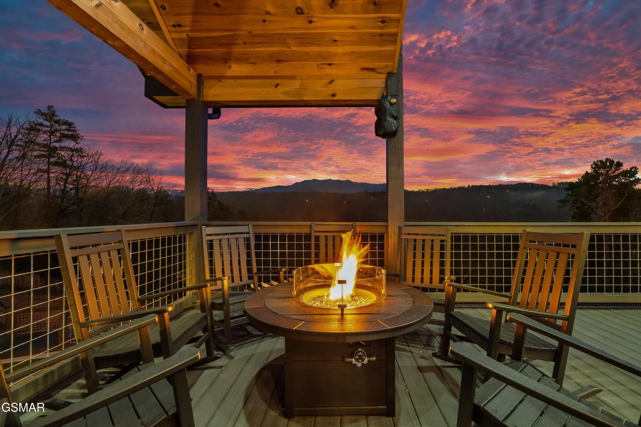 Mountain-view deck with a fire pit and wooden chairs beneath a timber roof at sunset.