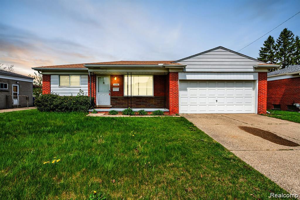 Single-story home with red brick accents, an attached garage, and a wide green lawn.