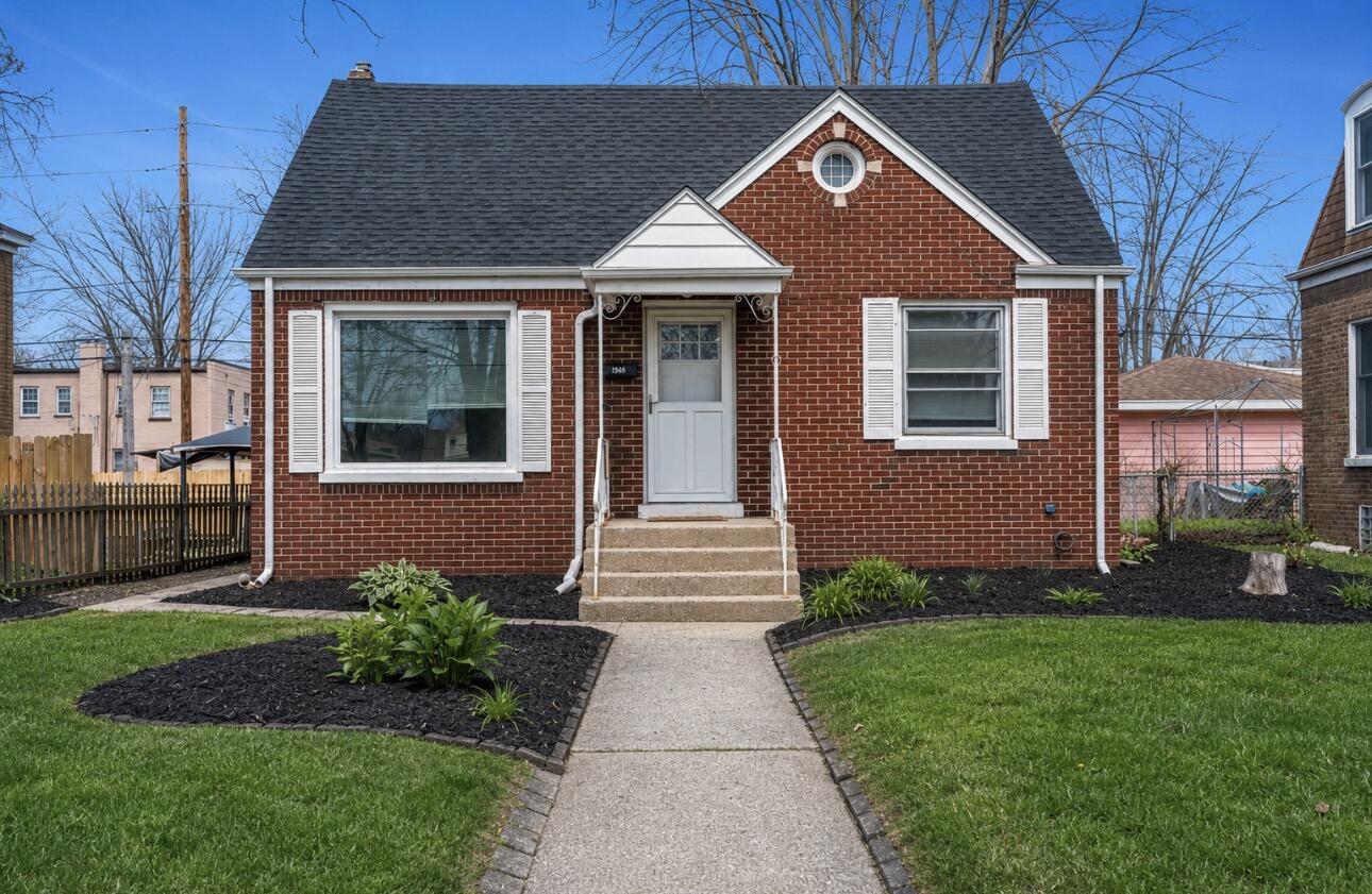 Red-brick house with white trim, a round attic window, and a walkway through the front lawn.