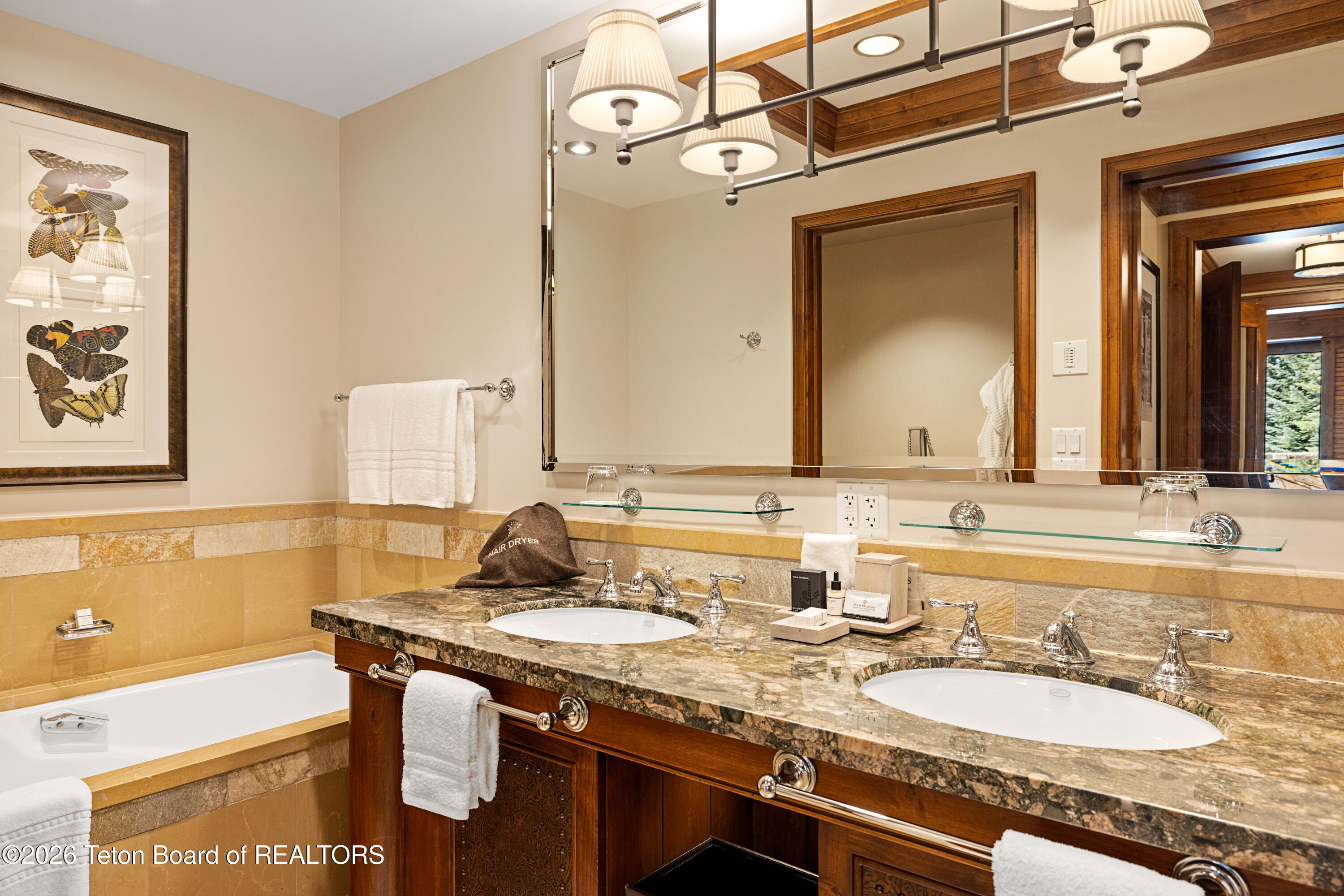 Bathroom with a double-sink stone vanity, wood cabinetry, and a tiled bathtub.