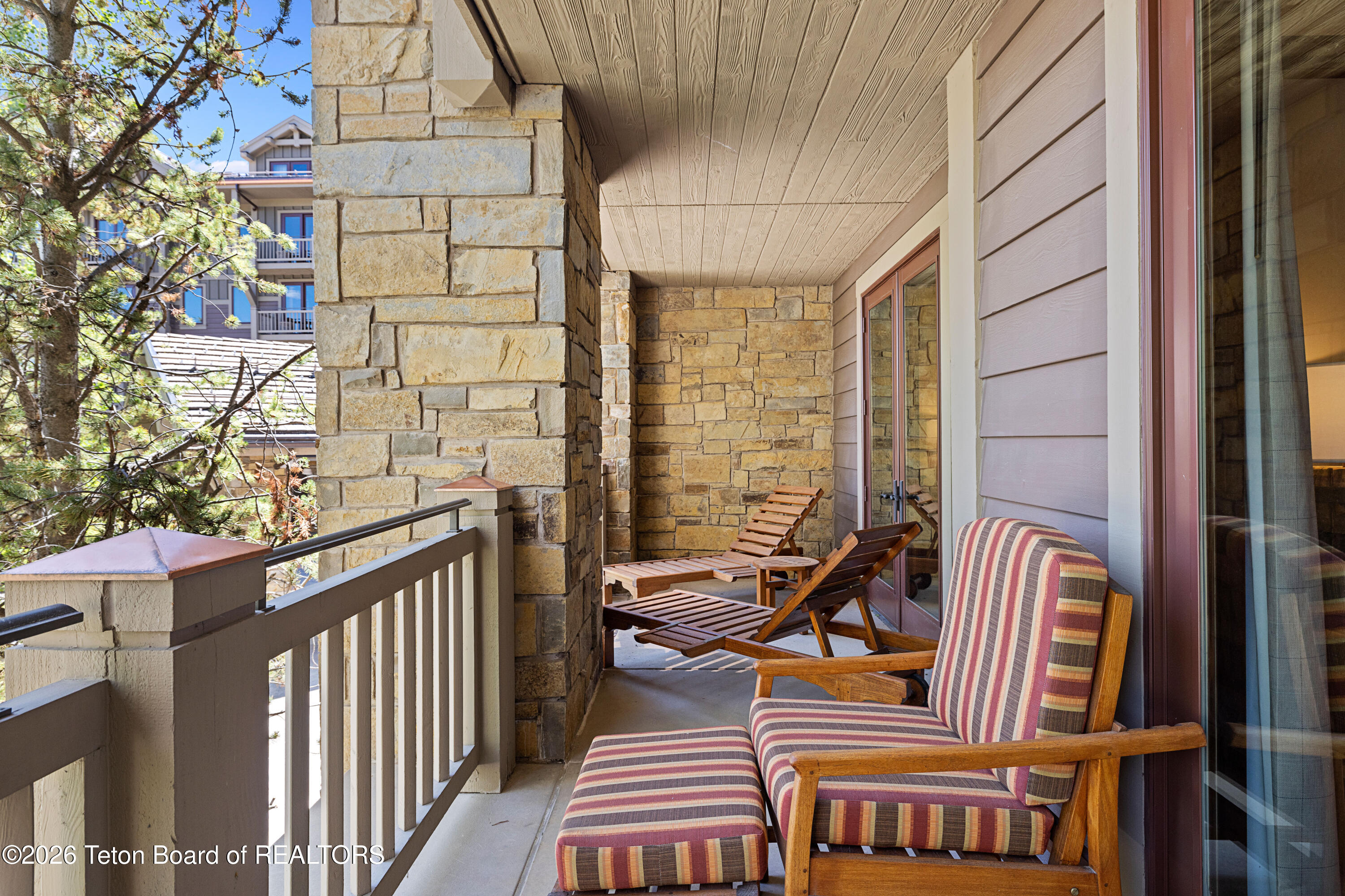 Covered balcony with stone walls, striped cushioned chairs, and wooden loungers.