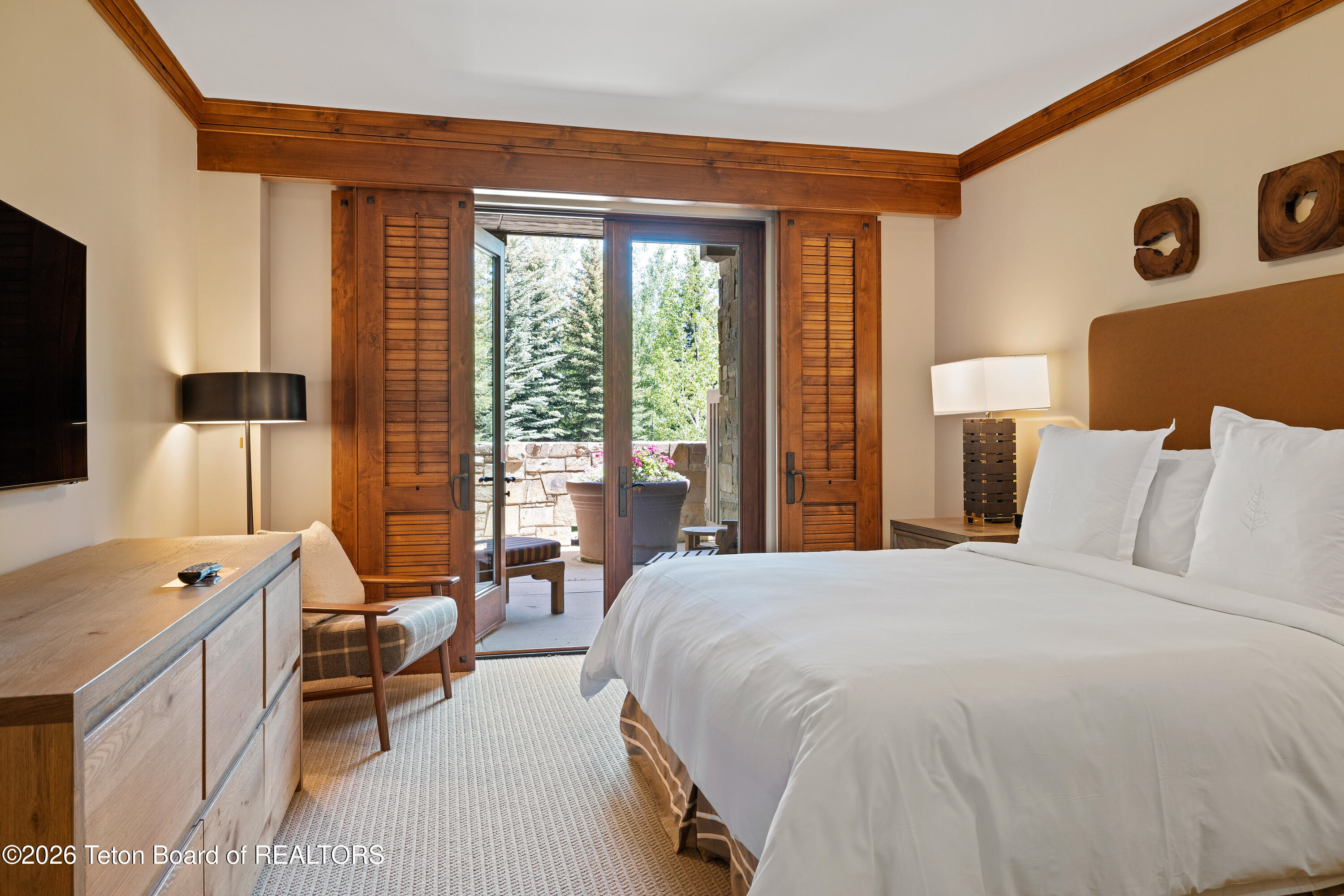 Bedroom with a white bed and wood-trimmed doors opening onto a stone patio.