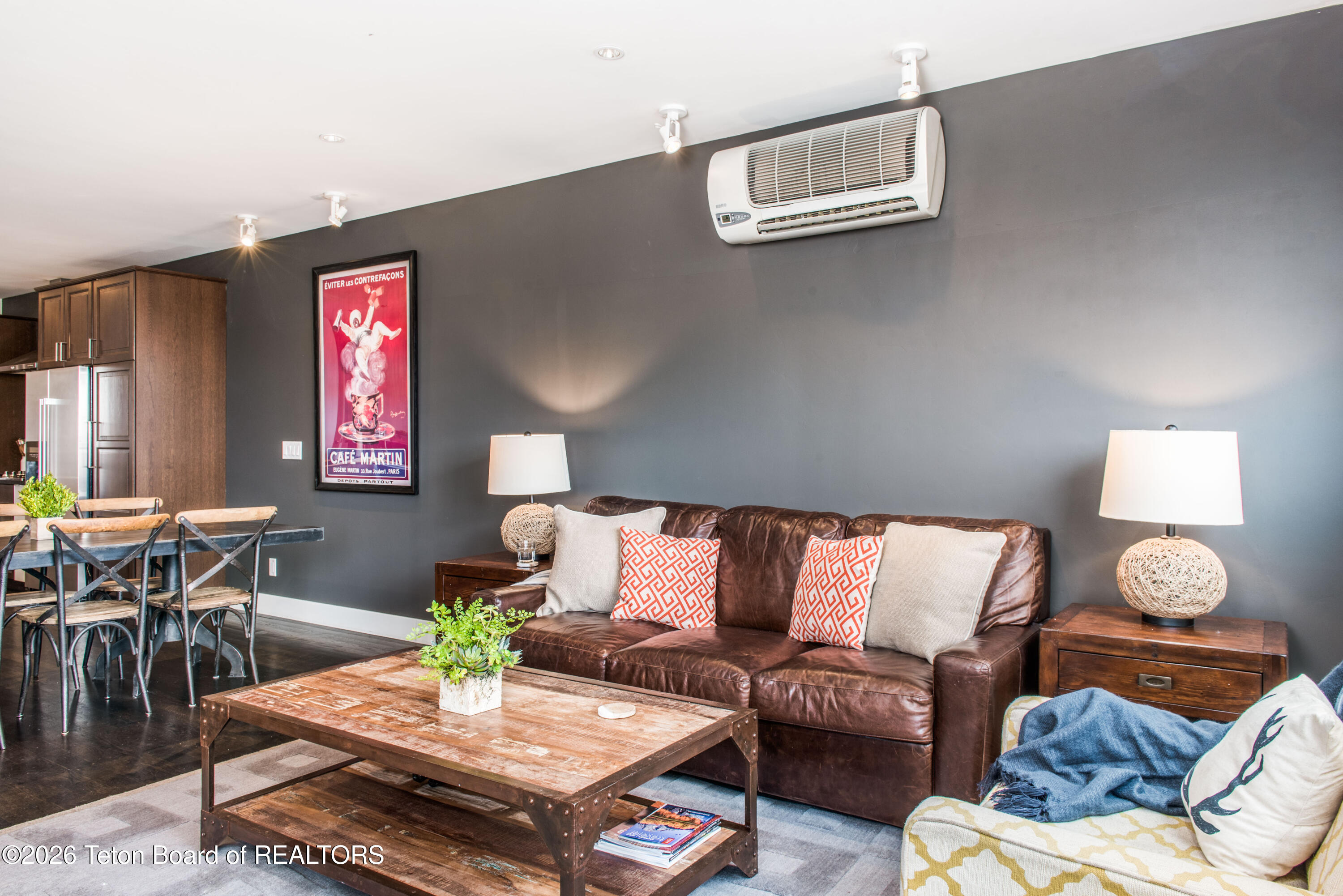 Living room with a brown leather sofa, patterned pillows, and a rustic wood coffee table beside the dining area.