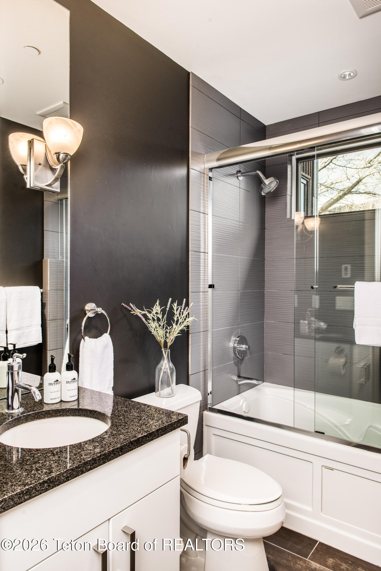 Modern bathroom with a glass-enclosed tub and shower beside a granite vanity.