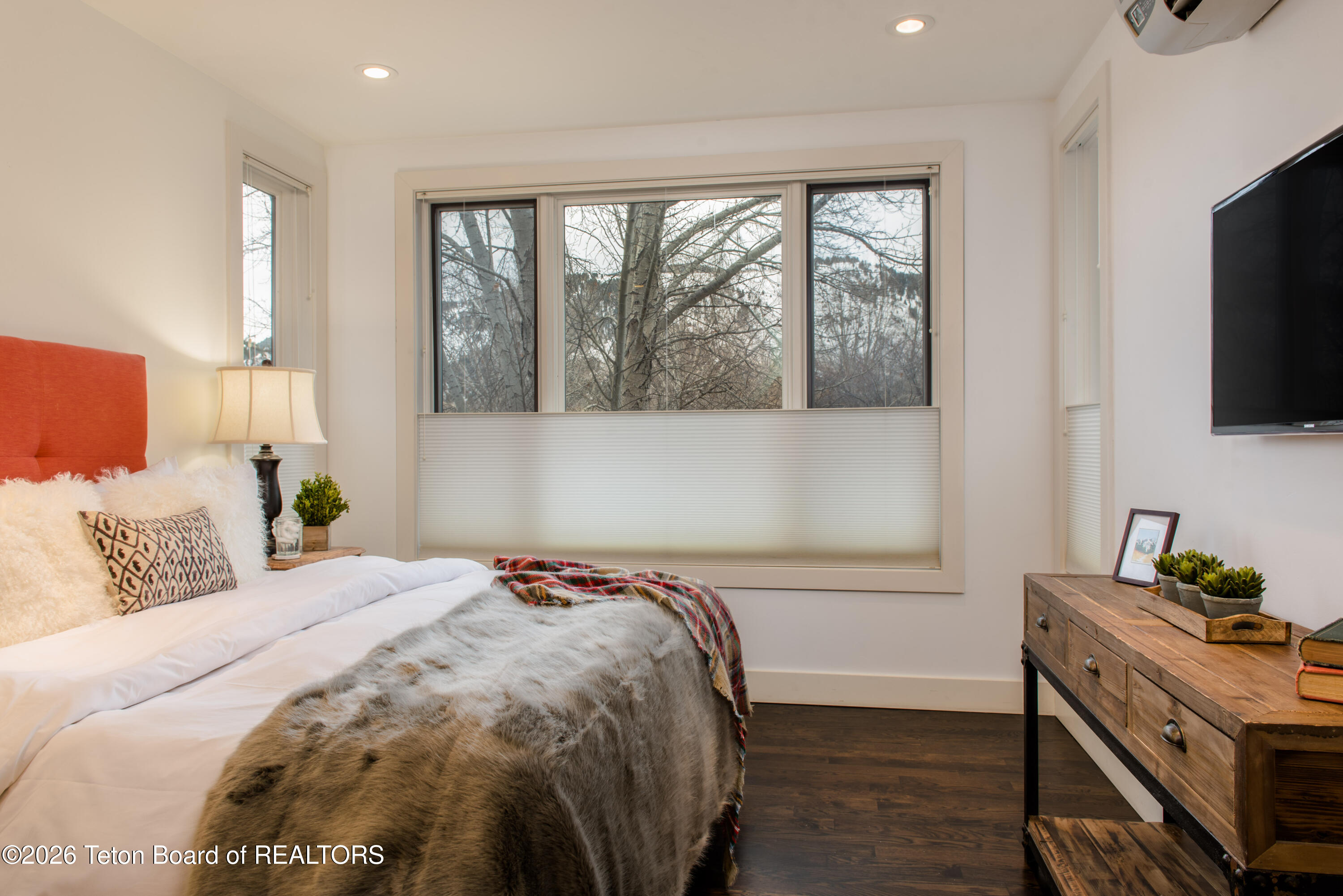 Bedroom with a red upholstered headboard, fur-style bed cover, and window overlooking a snowy landscape.