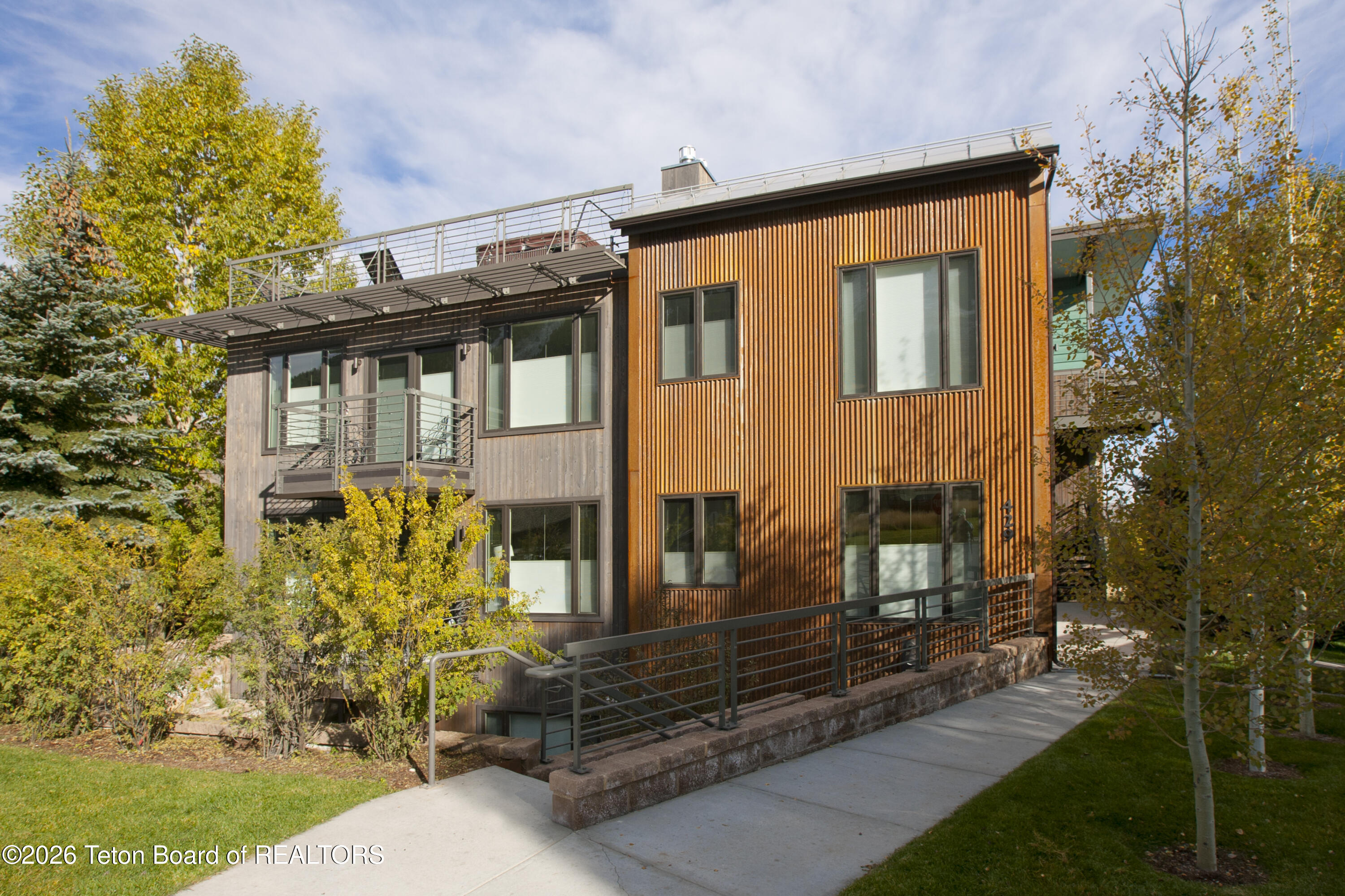 Modern wood-sided residence with rooftop deck and balconies among autumn trees.