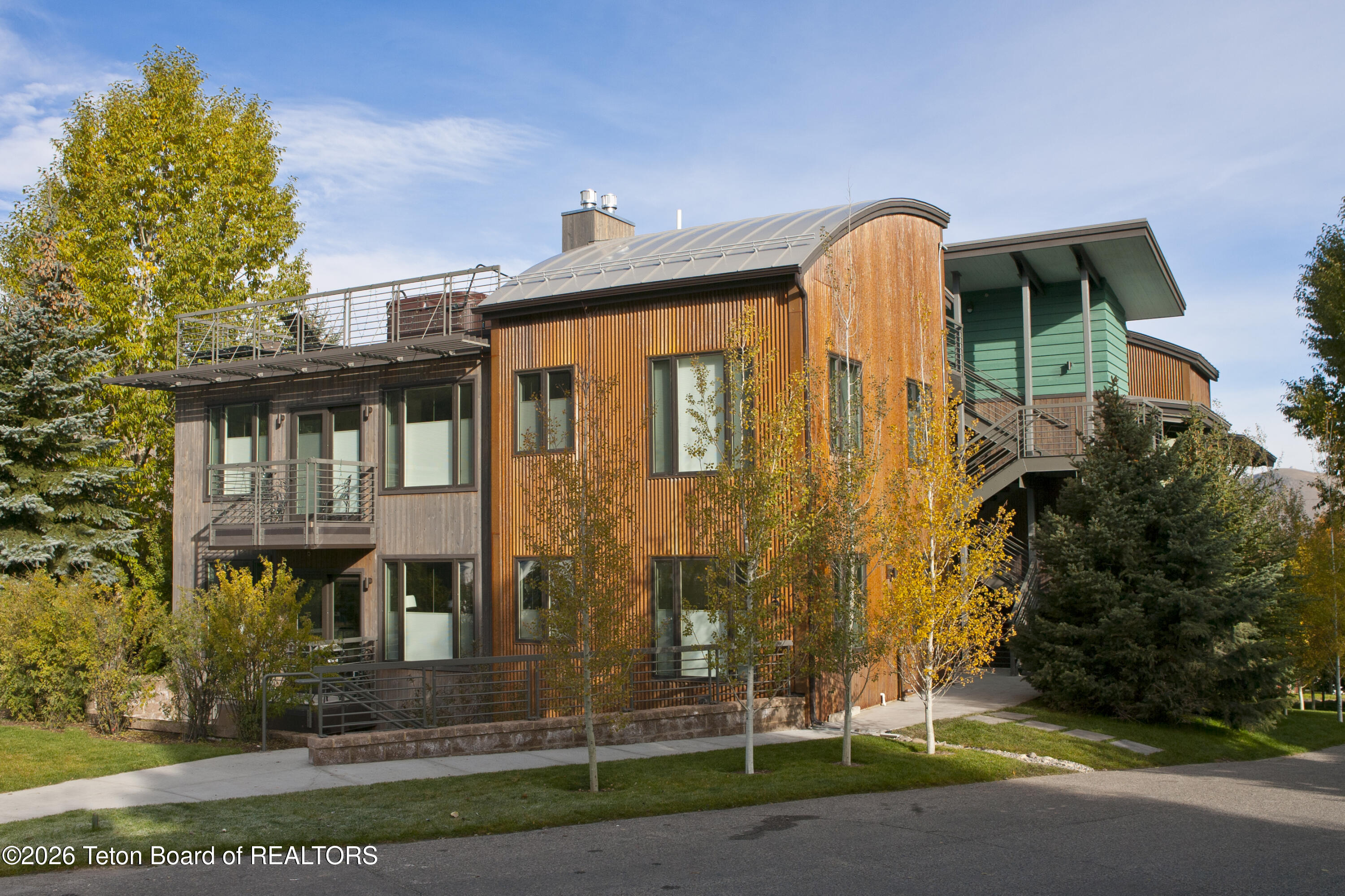 Modern multistory home with wood siding, balconies, and golden autumn trees.