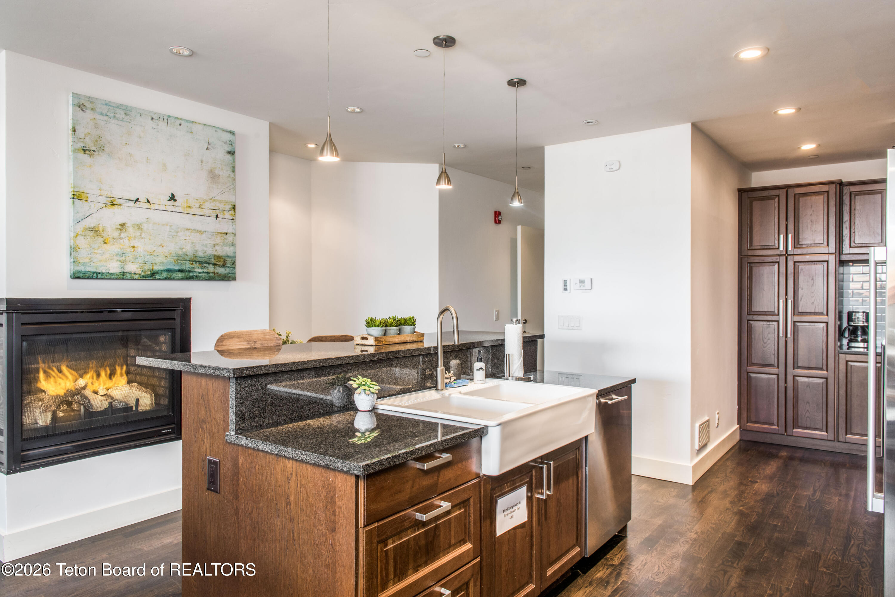 Kitchen with a granite island, farmhouse sink, dark wood cabinets, and a built-in fireplace.