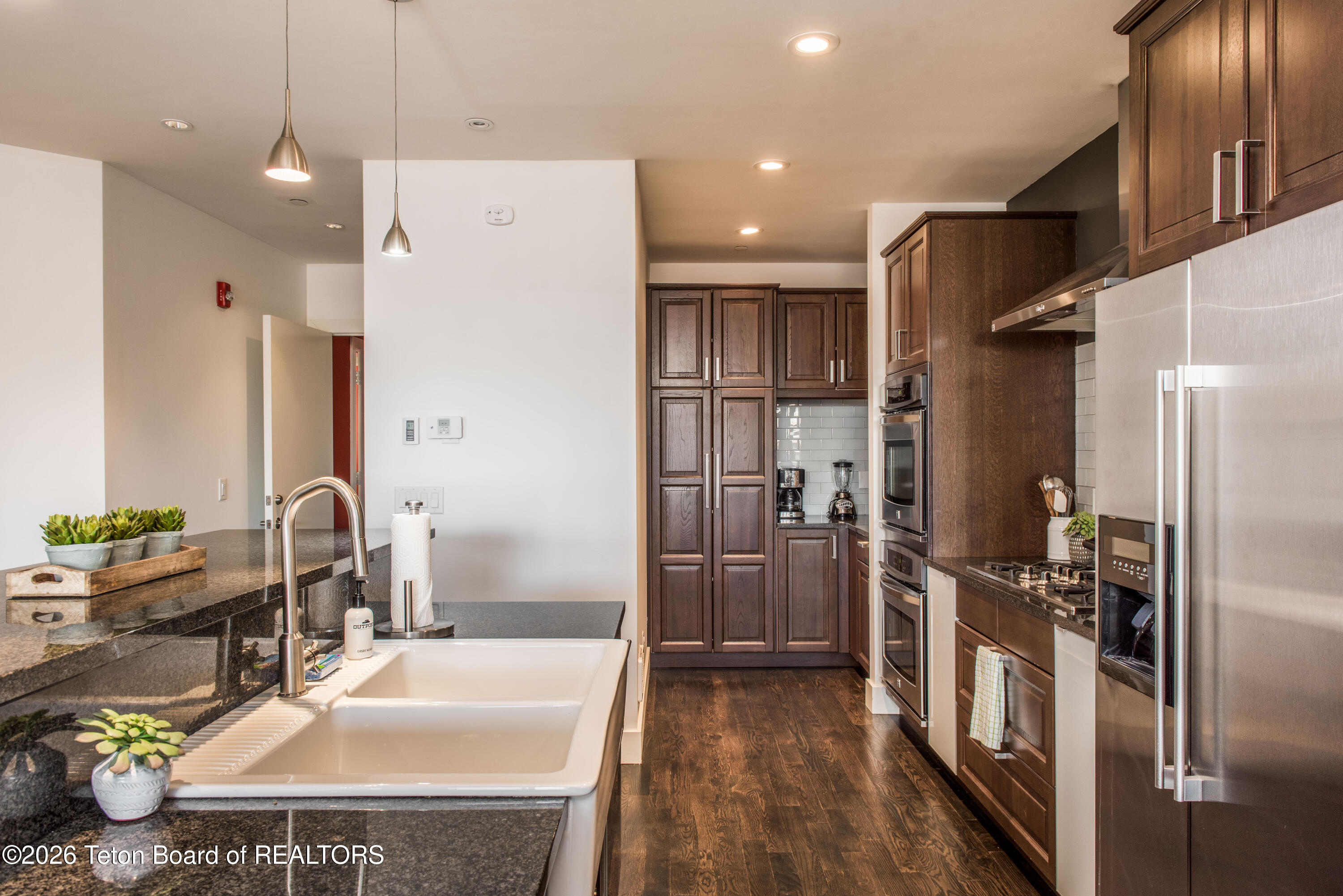 Modern kitchen with dark wood cabinetry, stainless steel appliances, and a granite island with farmhouse sink.