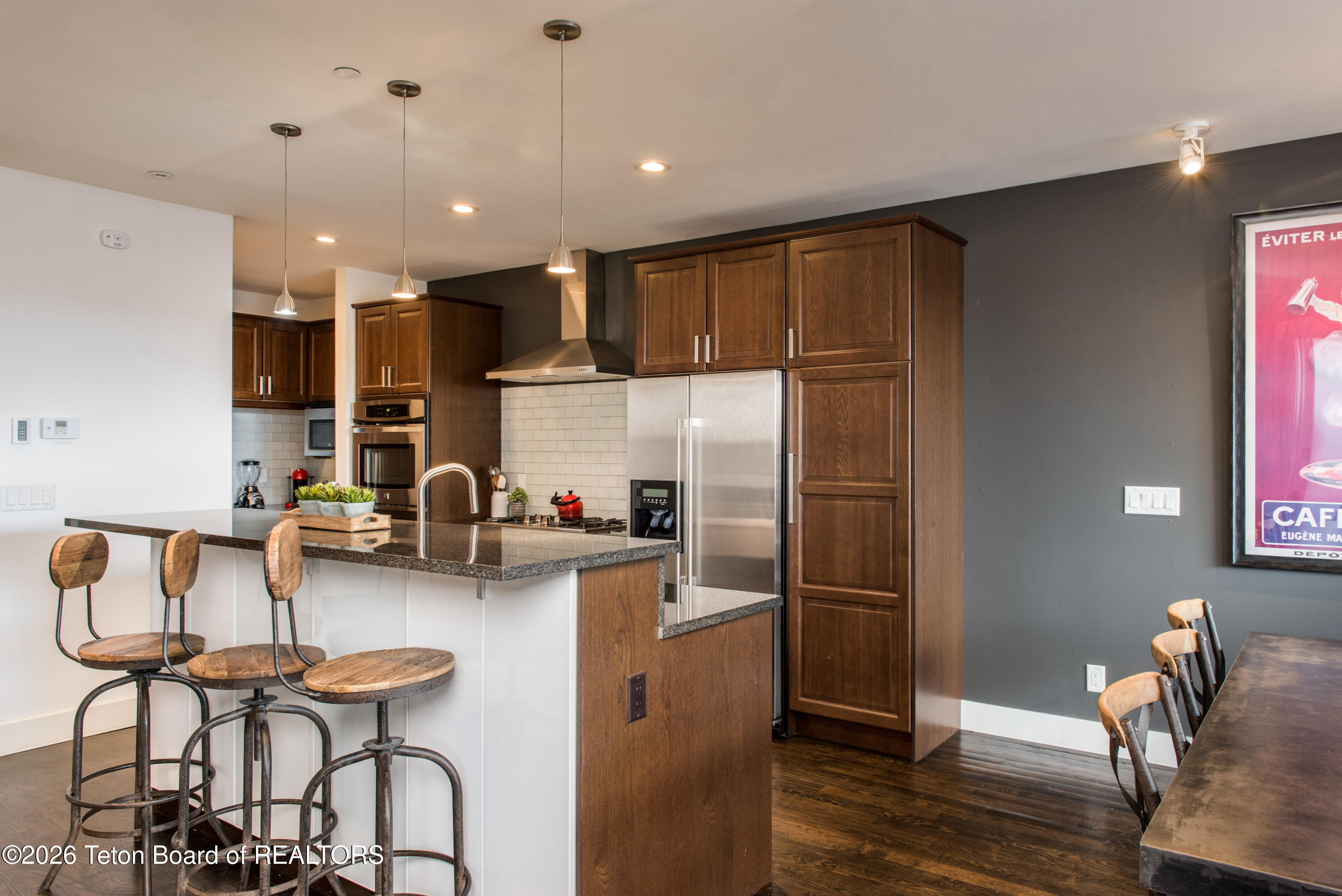 Kitchen with dark wood cabinets, stainless steel appliances, and a granite island with three wooden bar stools.