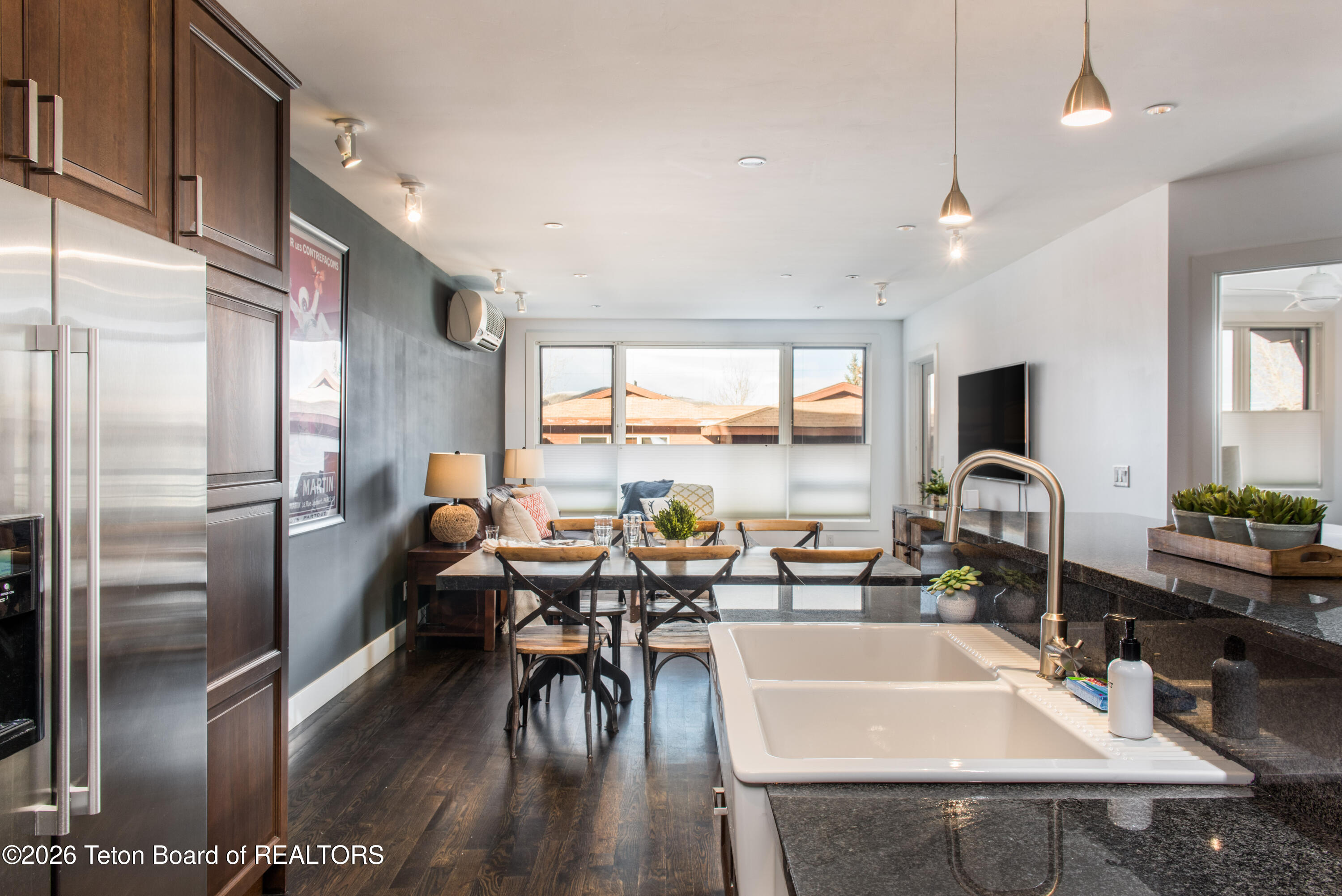 Kitchen and dining area with a large farmhouse sink, dark granite counters, and windows overlooking rooftops.