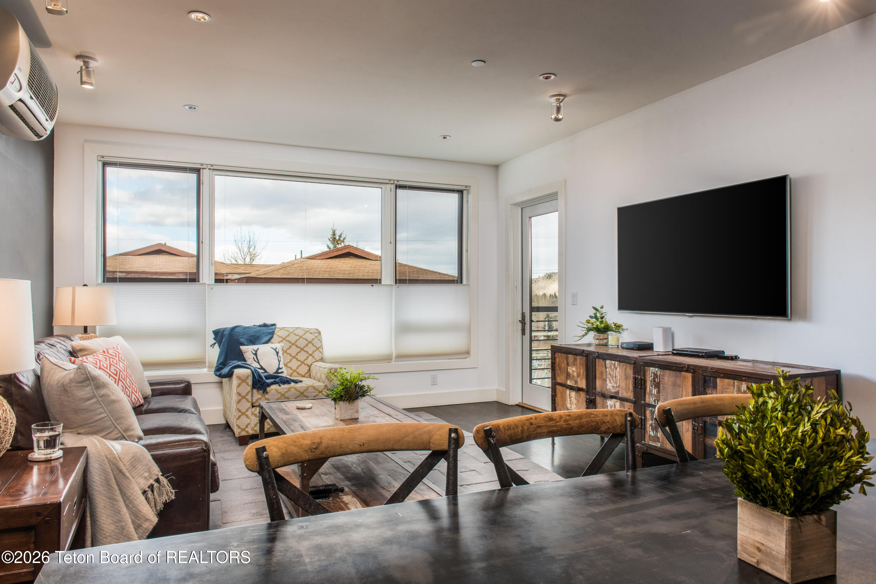 Furnished living room with a leather sofa, patterned armchair, and large windows.