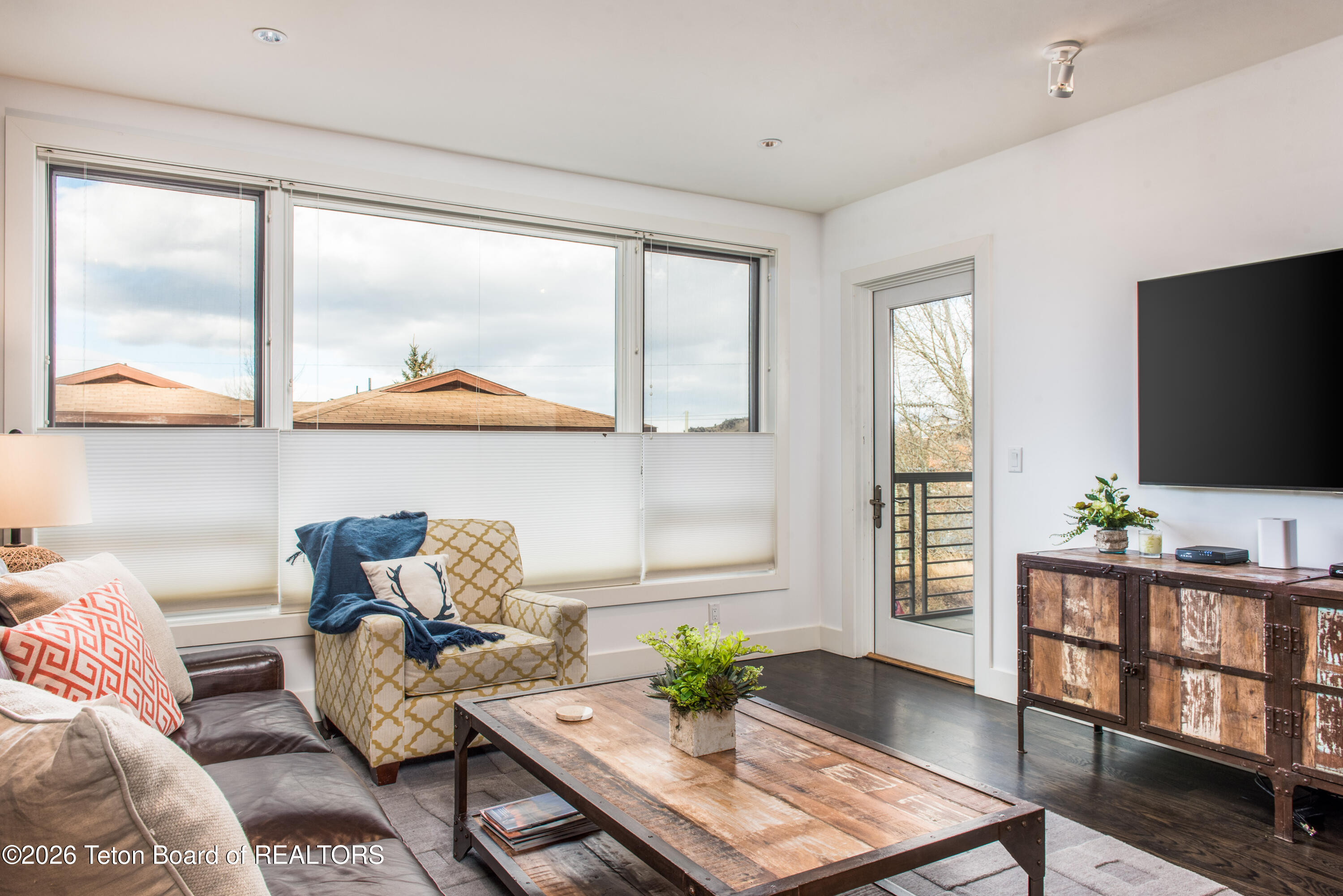 Living room with large windows, a patterned armchair, and a rustic wood coffee table.