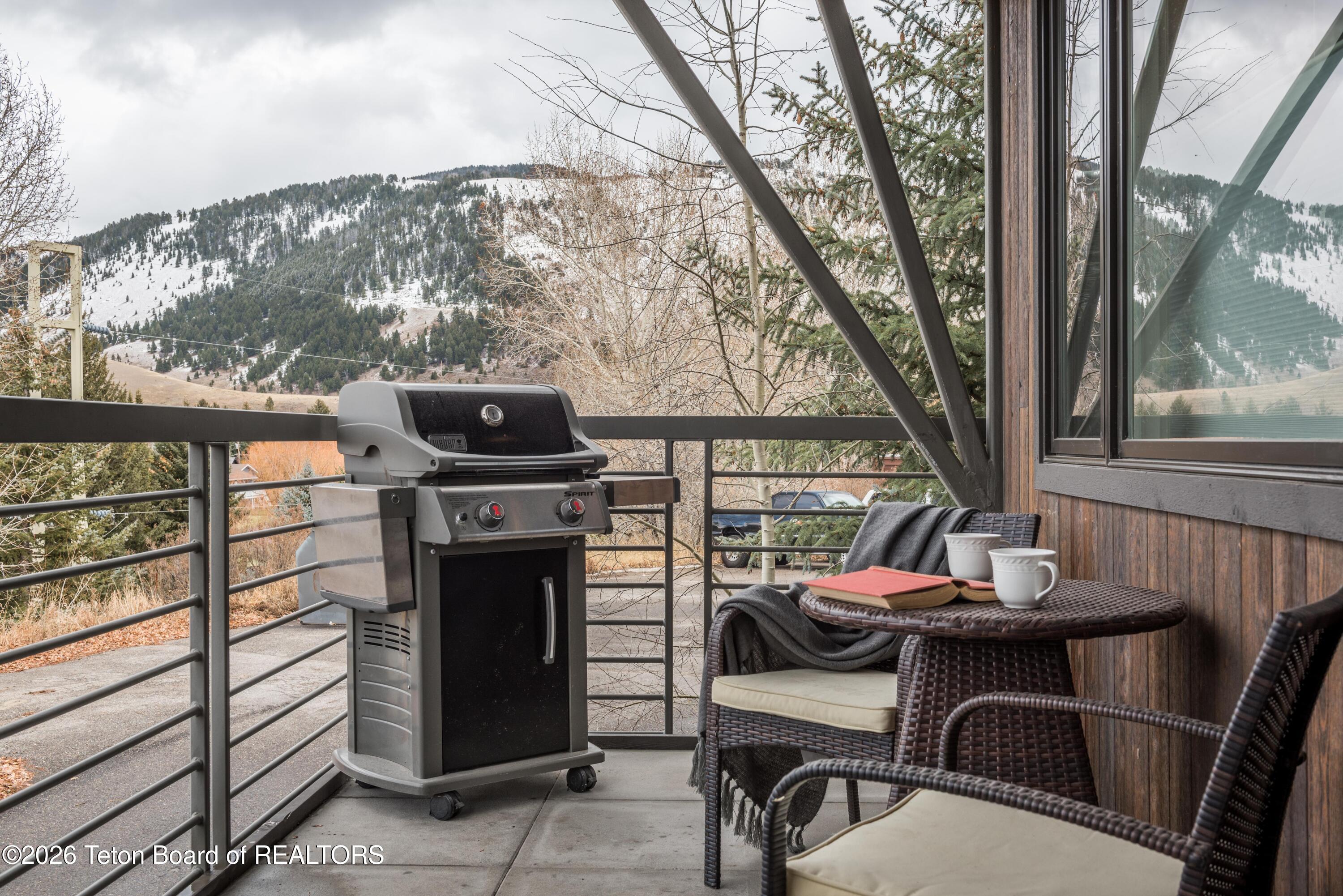 Mountain-view deck with a gas grill and wicker seating.