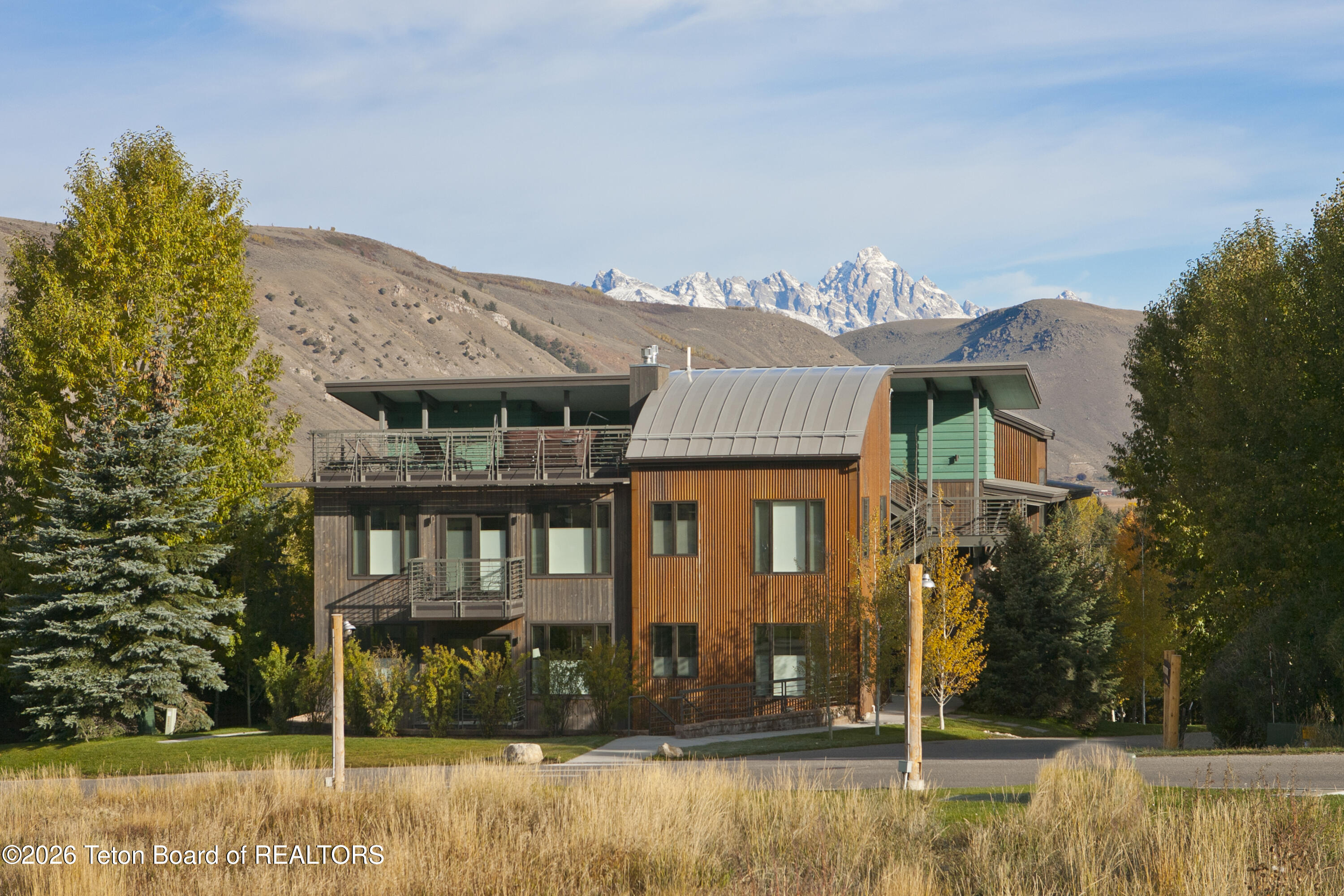 Modern home with green and rust siding, set against the snow-capped Teton Range.