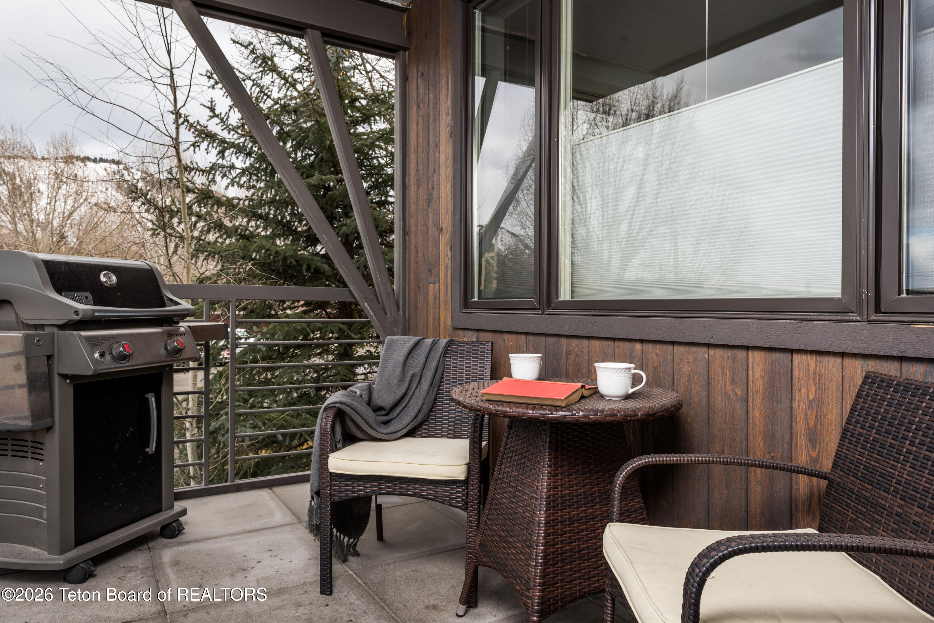Outdoor balcony with a gas grill and wicker seating around a small table.