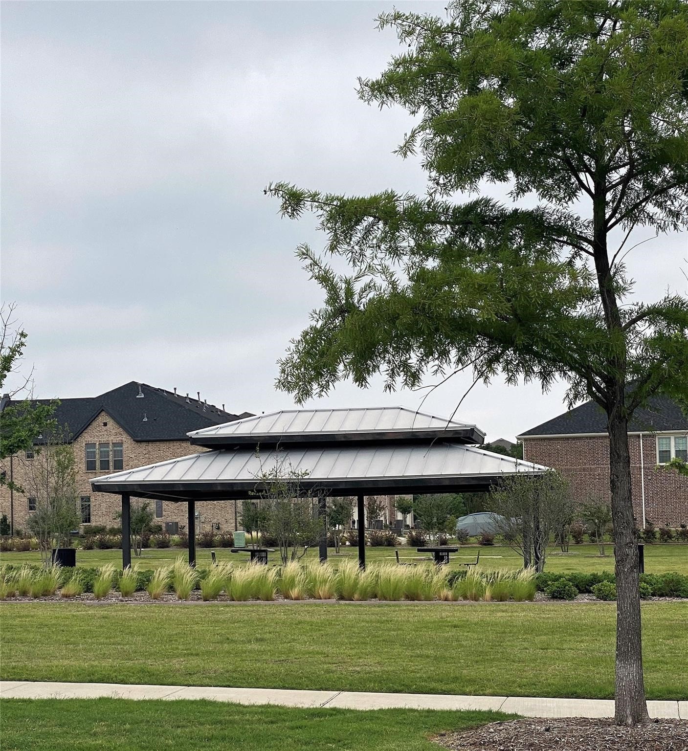 Neighborhood park pavilion with a two-tier metal roof, picnic tables, and surrounding homes.