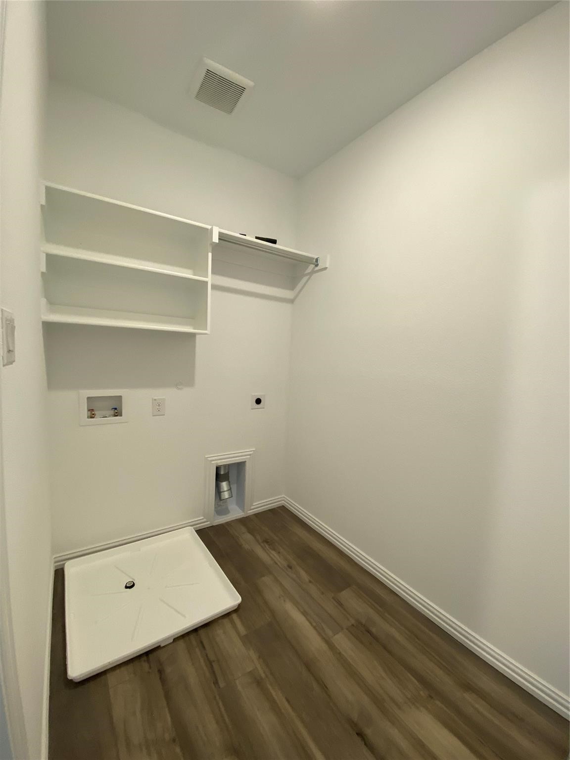 Empty laundry room with upper storage shelves, washer hookups, and a white drain pan.