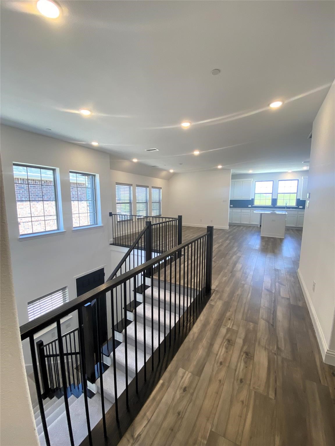 Upstairs landing with a black-railed staircase, wood-look flooring, and kitchen beyond.