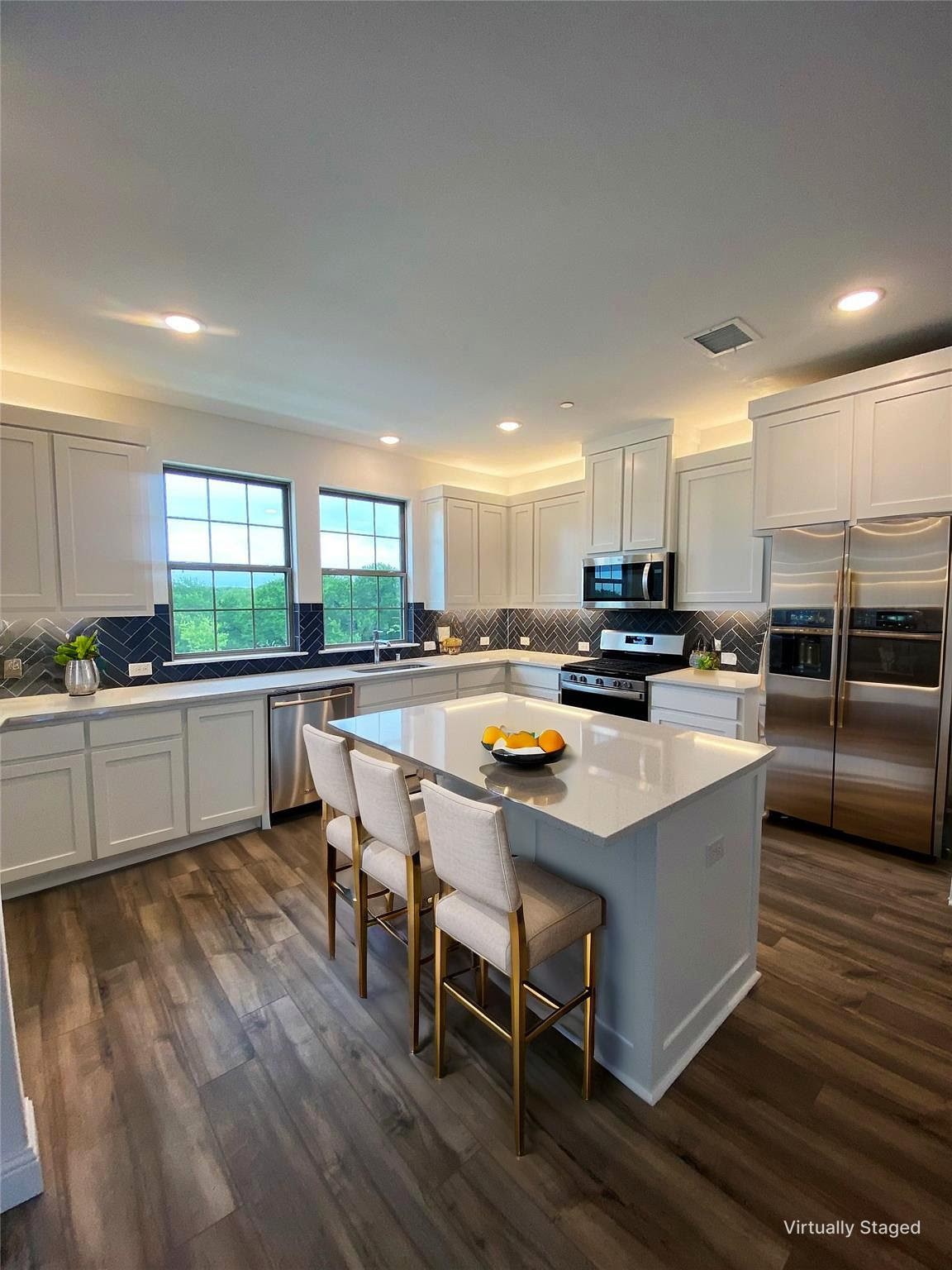 Kitchen with a large island, white cabinetry, dark herringbone backsplash, and stainless steel appliances.