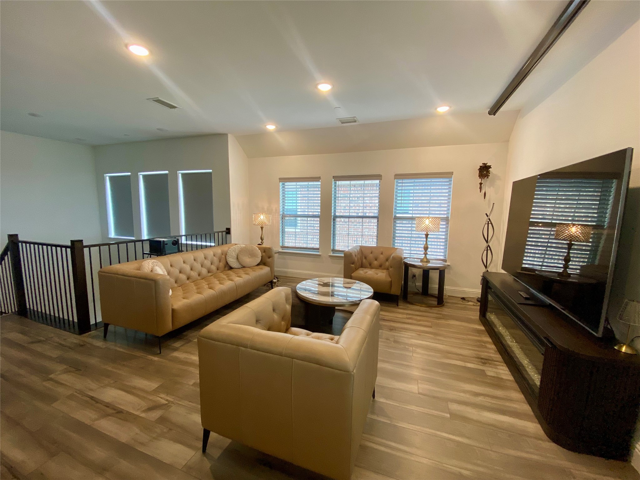 Furnished living room with tan tufted seating, wood-look floors, and a large television.