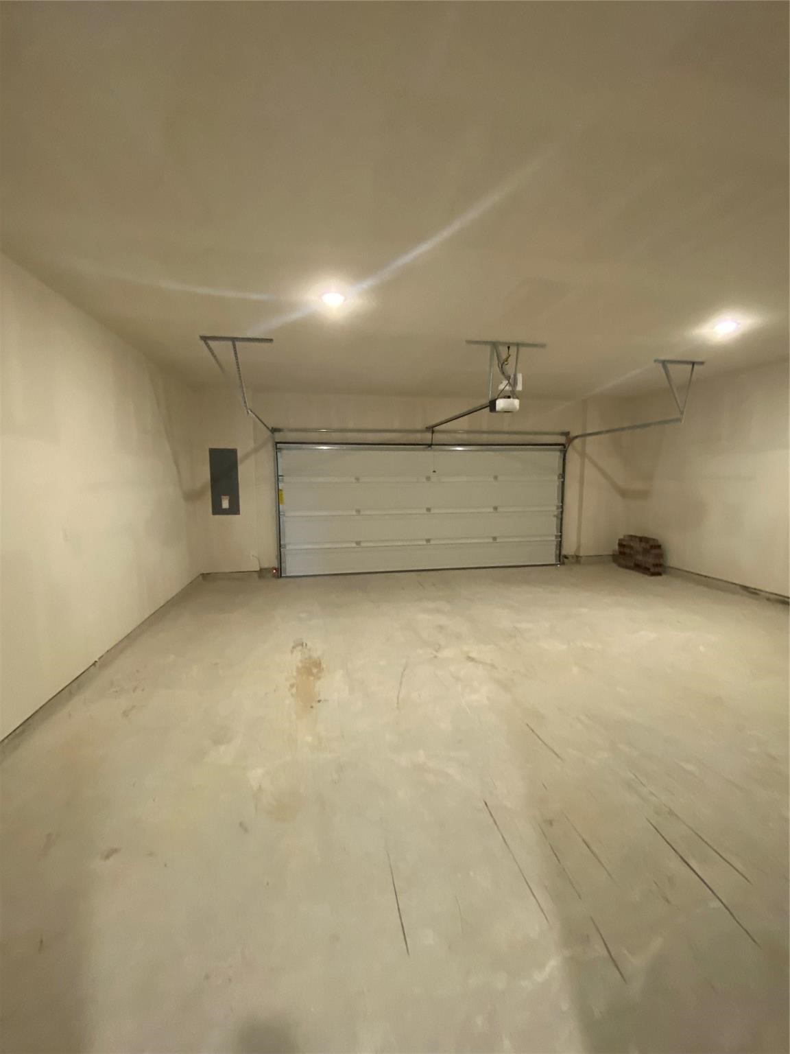 Empty garage with a closed sectional door, overhead opener, and bare concrete floor.