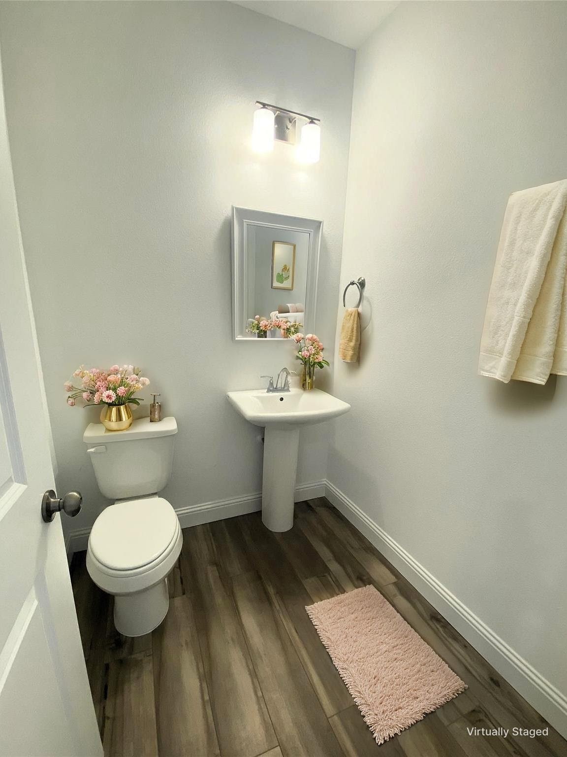 Bathroom with a pedestal sink, toilet, framed mirror, and pink floral accents.
