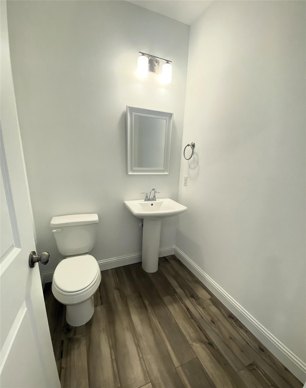 Unfurnished bathroom with a pedestal sink, toilet, and dark wood-look plank flooring.