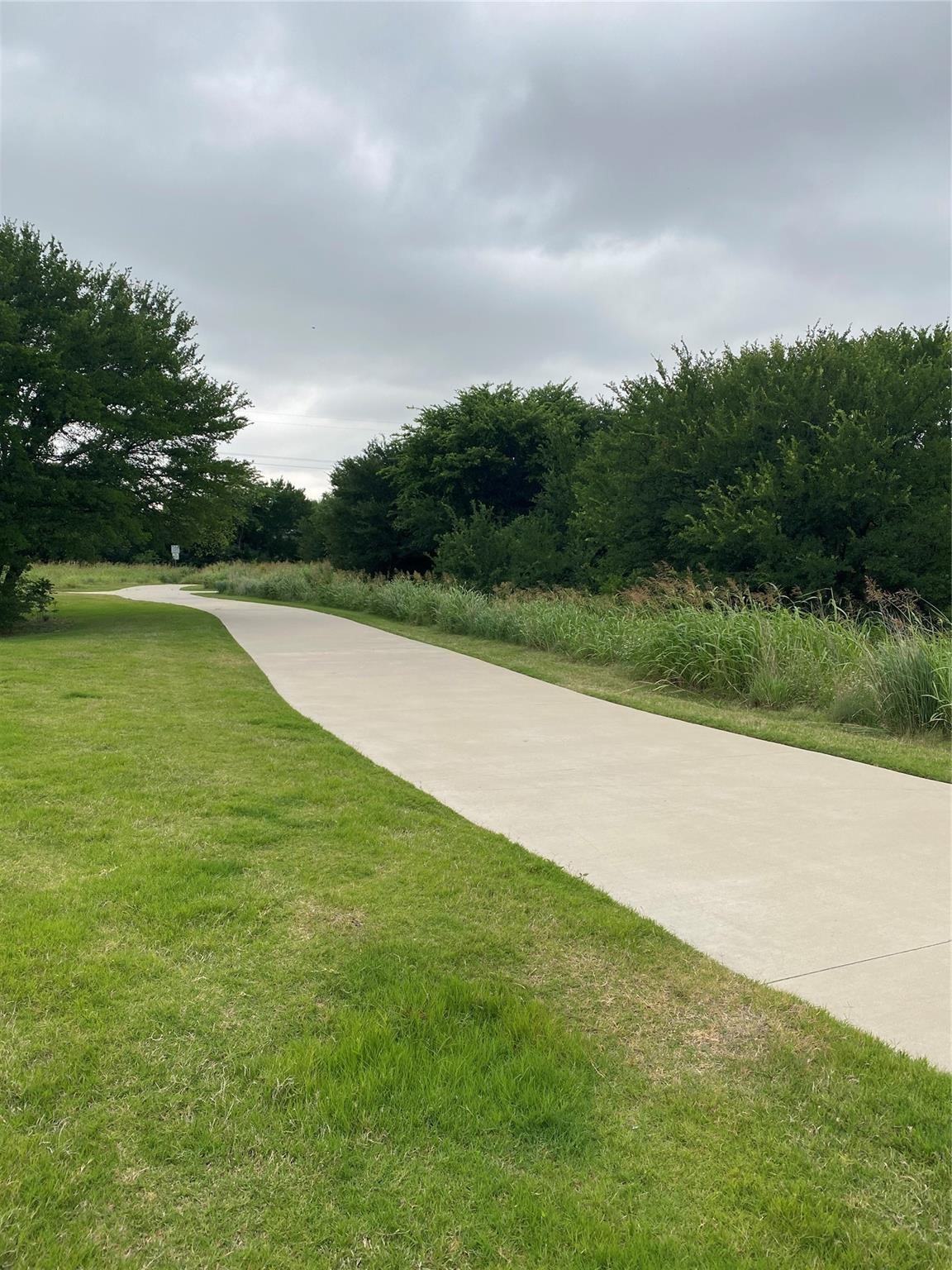 Concrete walking path curving through a grassy, tree-lined greenway.