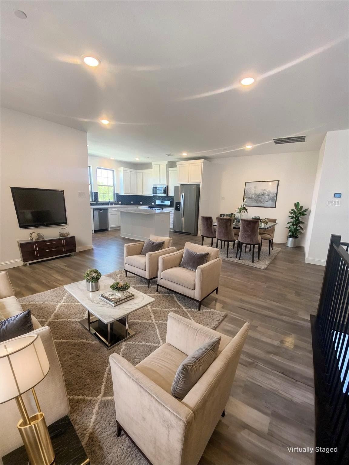 Open-plan living room with cream armchairs, patterned rug, and adjoining kitchen with white cabinets and stainless appliances.