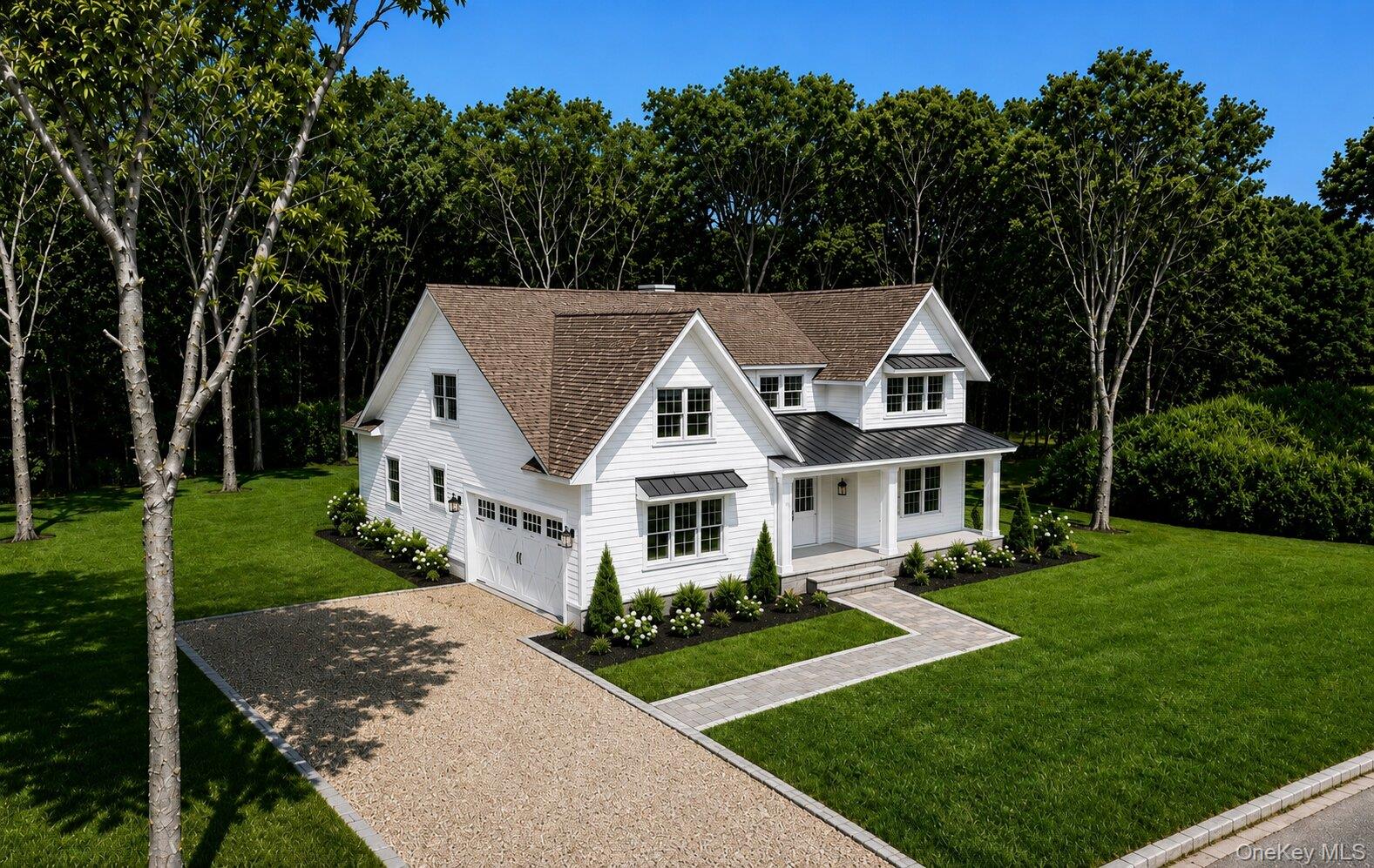 White gabled house with a covered porch, attached garage, landscaped lawn, and gravel driveway.