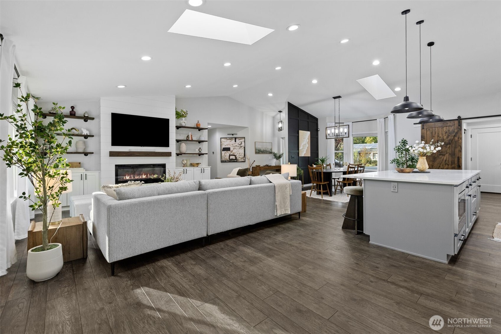 Open-plan living room and kitchen with a gray sectional, fireplace, and large white island.
