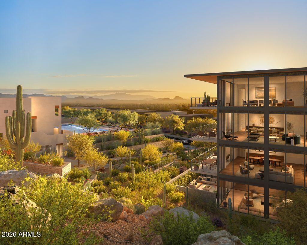 Modern glass residence overlooking landscaped desert grounds and mountains at sunset.