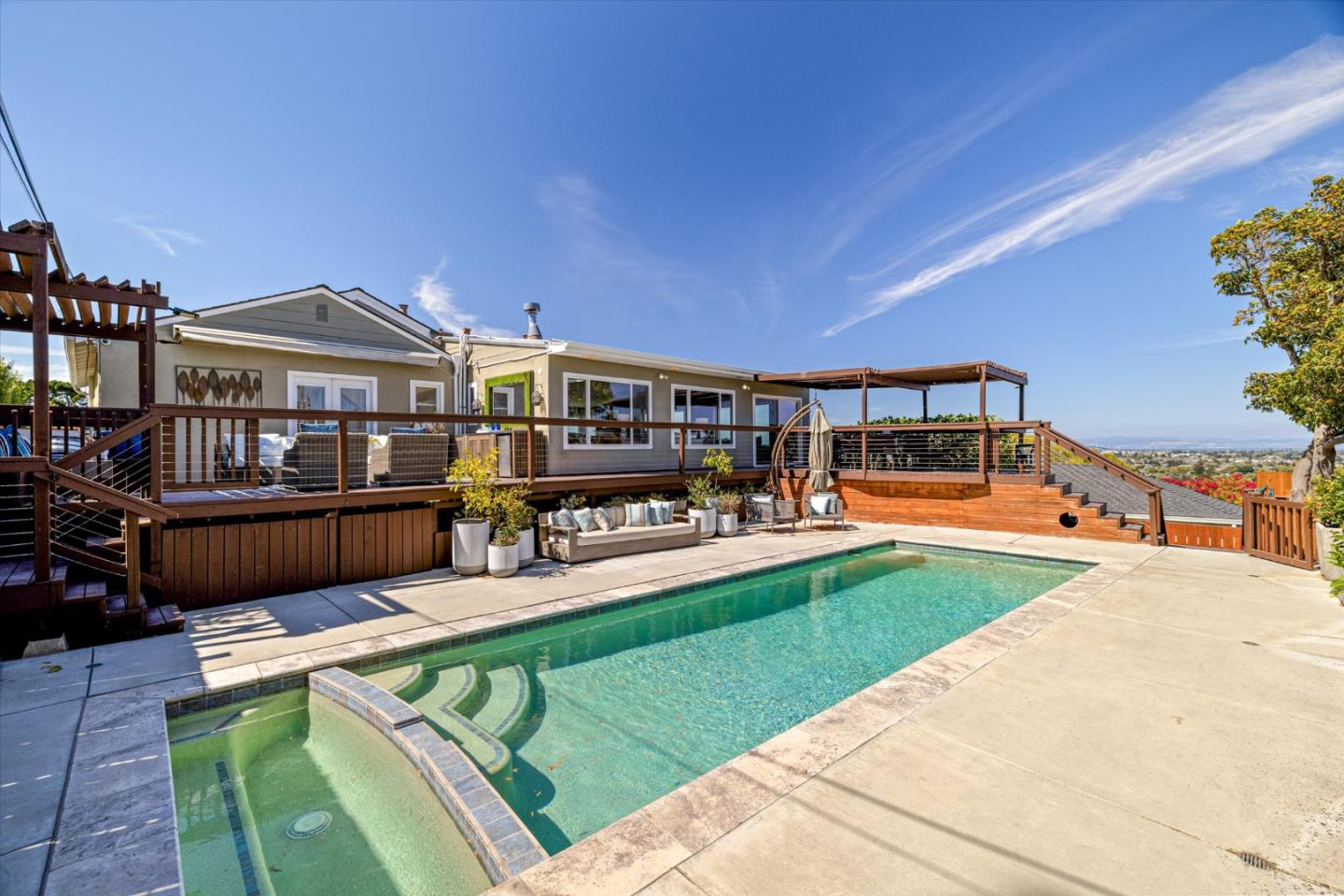 Home with a wide wood deck, outdoor seating, and a swimming pool with attached spa.